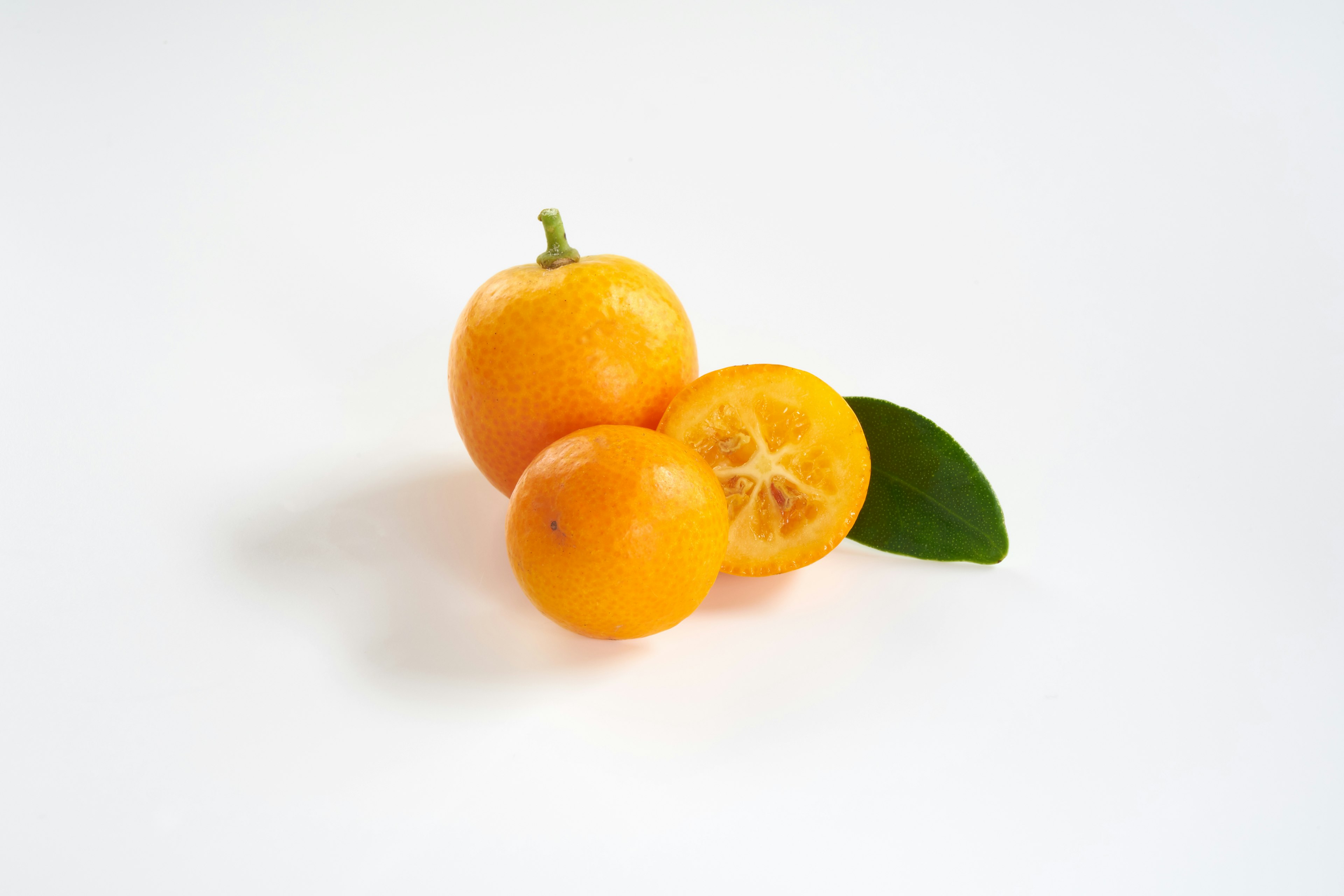 Tres frutas cítricas naranjas dispuestas con una hoja verde sobre un fondo blanco