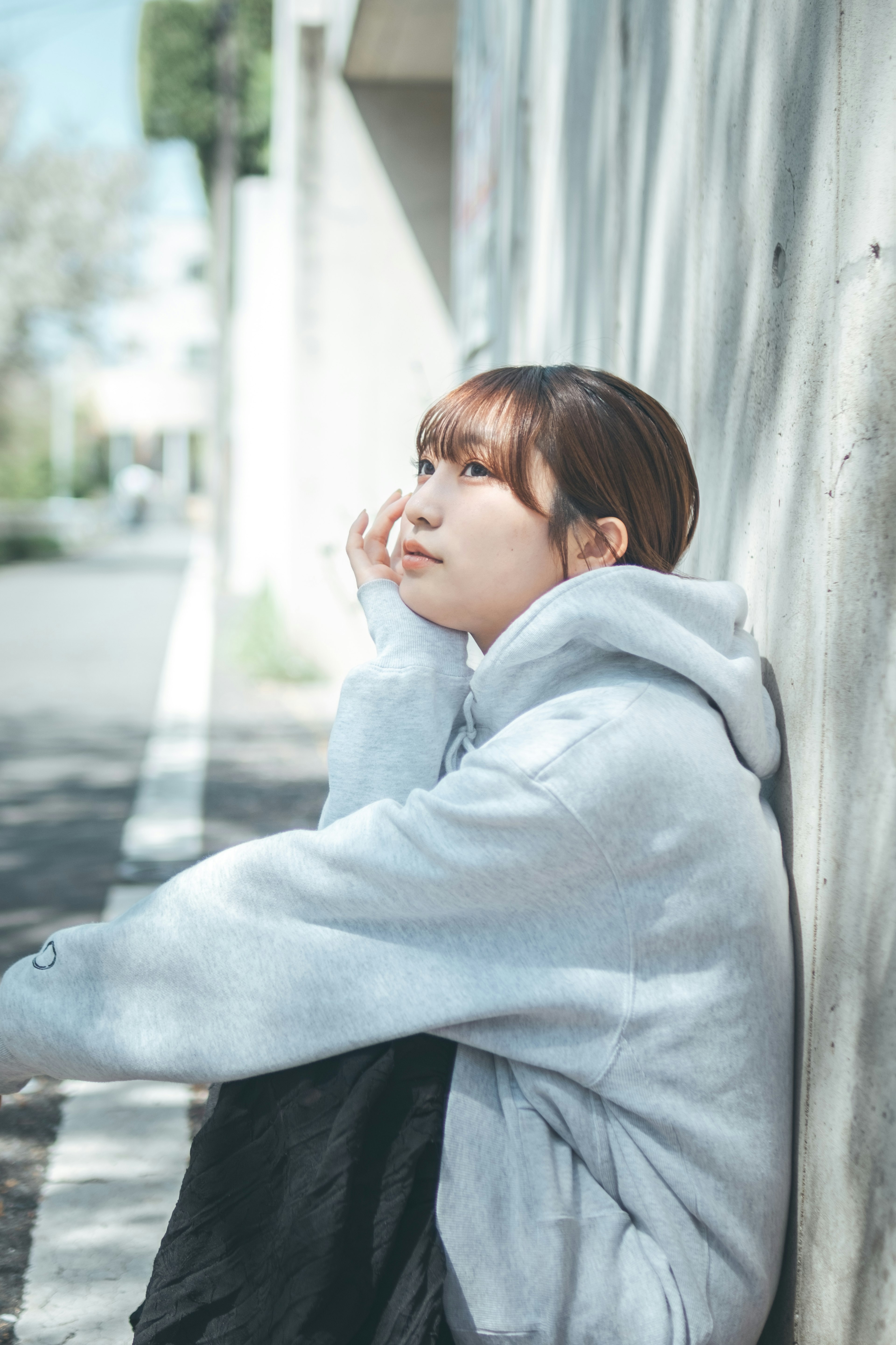 A woman sitting against a wall looking thoughtful