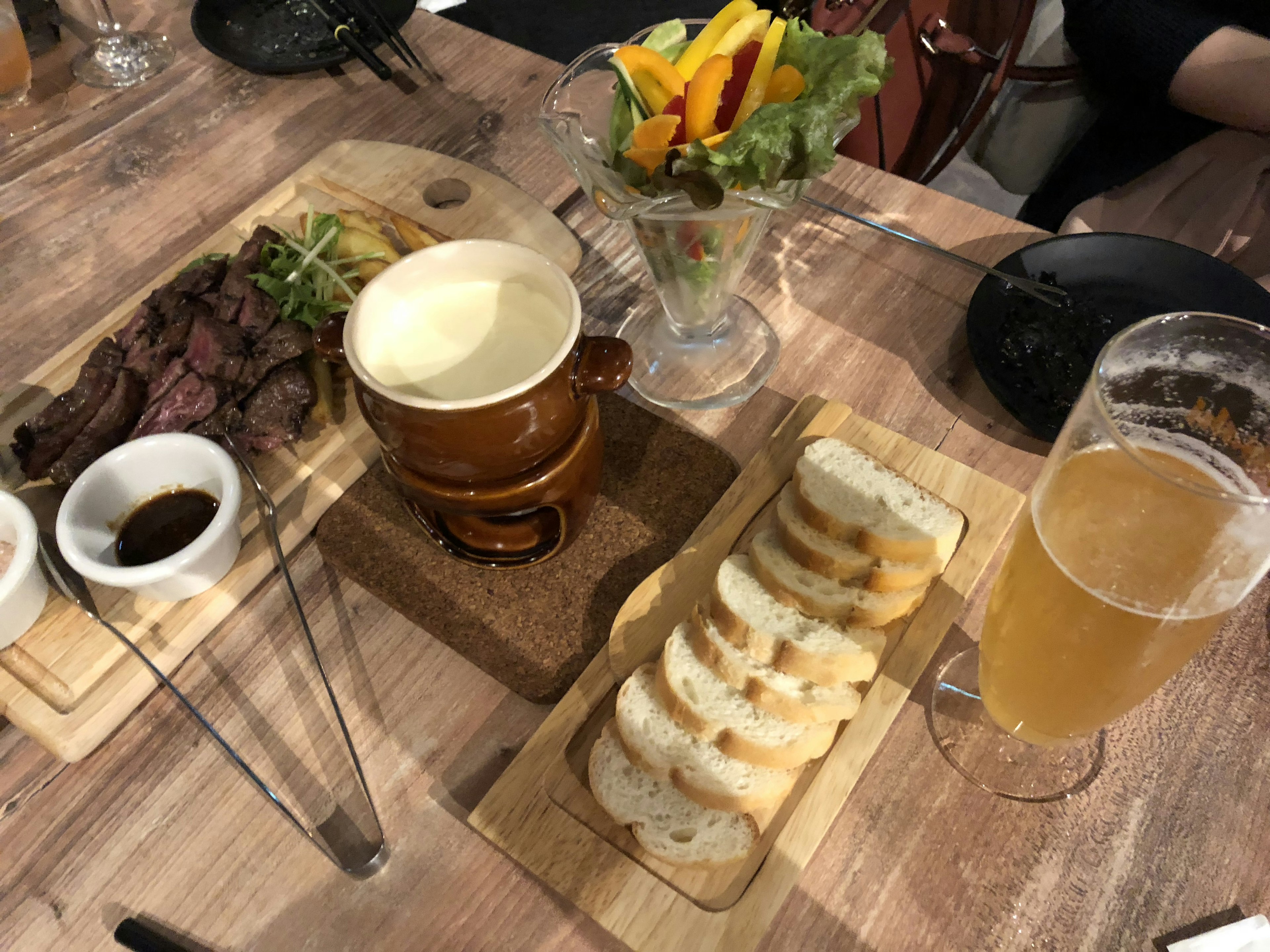 A table setting featuring delicious dishes and drinks including steak, bread, salad, beer, and sauce