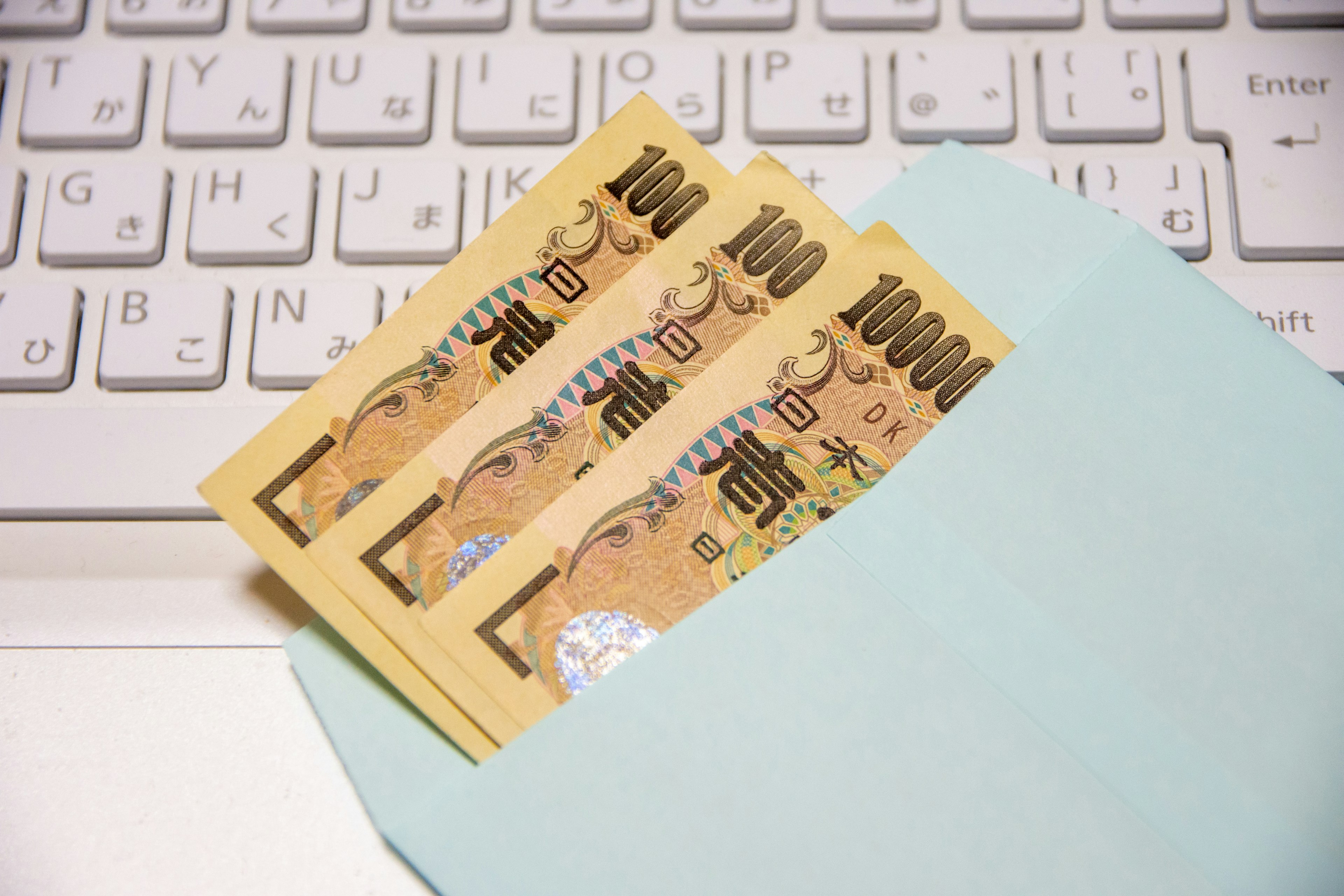 Tres billetes de 10,000 yen colocados sobre un sobre azul claro junto a un teclado