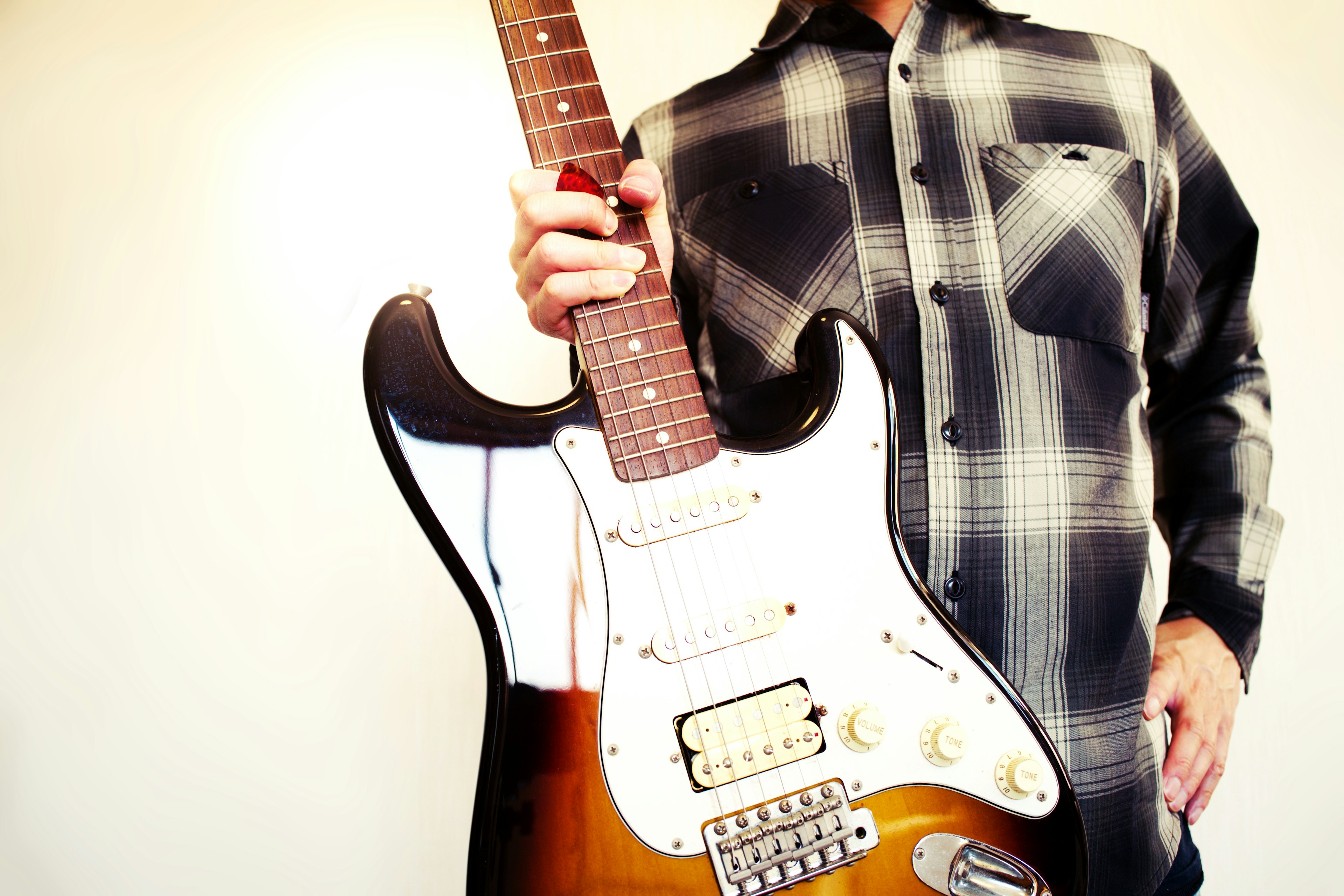 Man holding a guitar wearing a checkered shirt