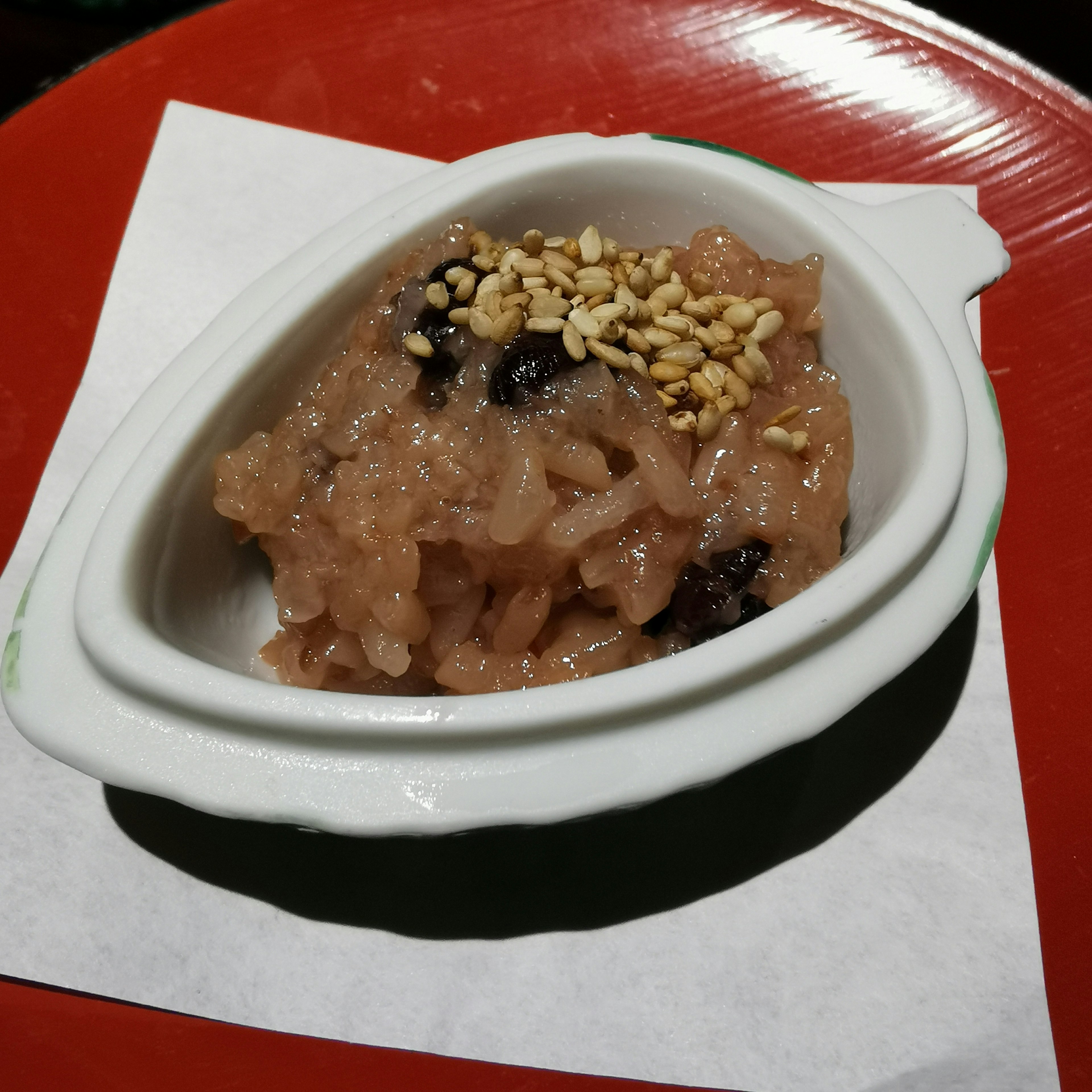 Sweet dessert served in a small white dish topped with sesame seeds and made of sticky rice