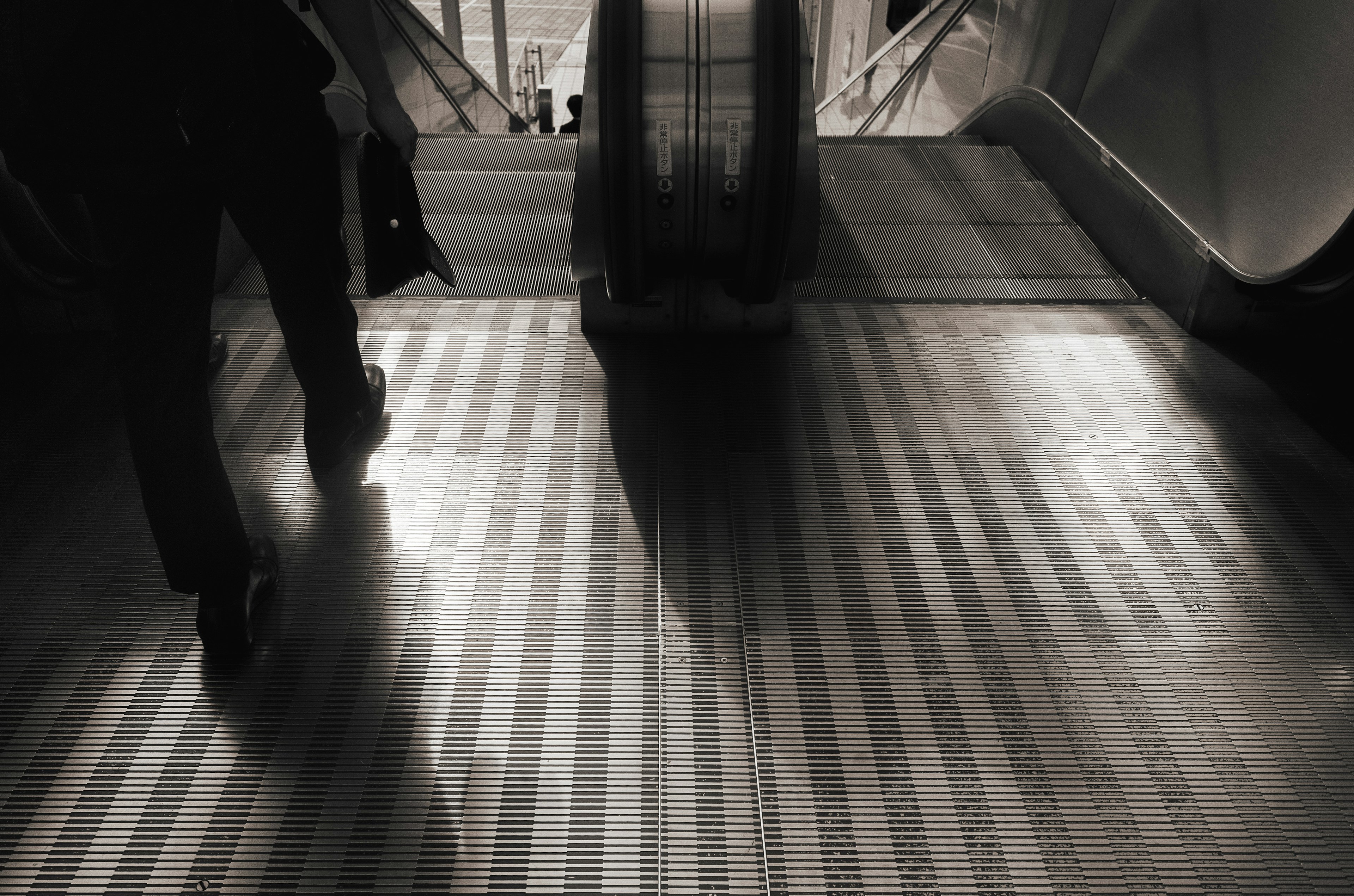 Person walking down an escalator with shadow and textured floor