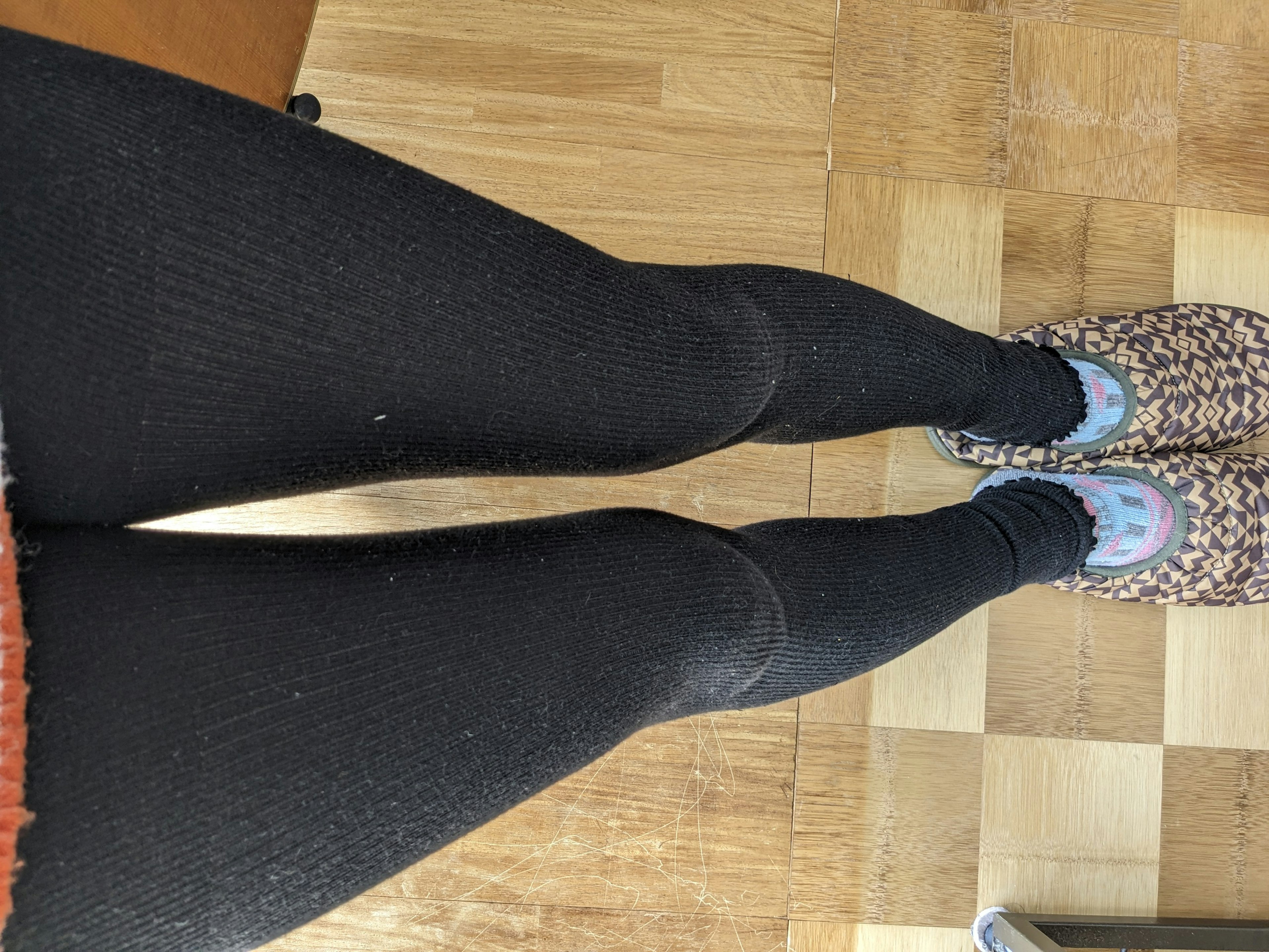 Bild von Beinen in schwarzen Leggings und bunten Hausschuhen