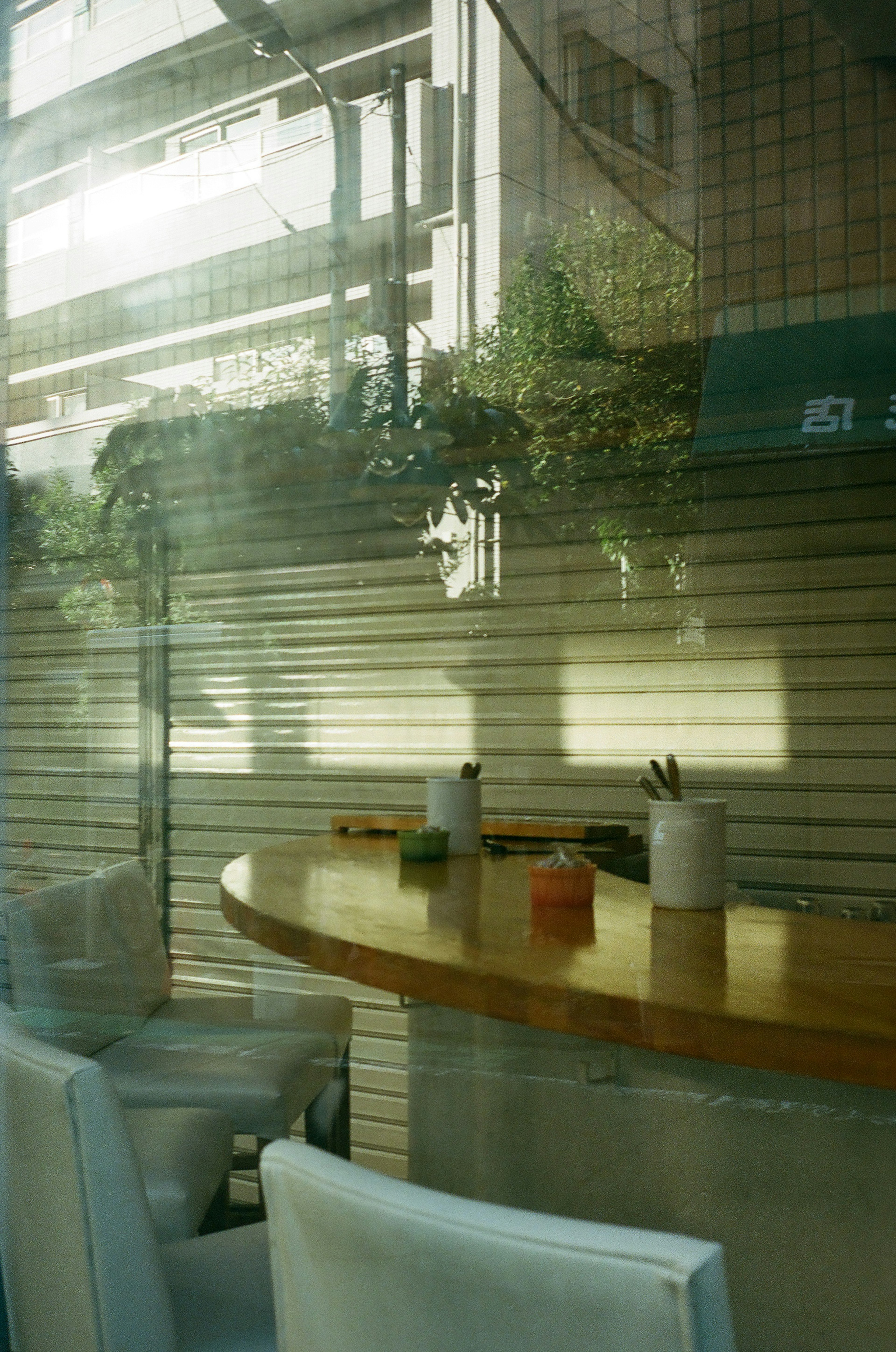 Interior brillante de una cafetería con mesa de madera y sillas blancas Sombras de edificios visibles a través de la ventana