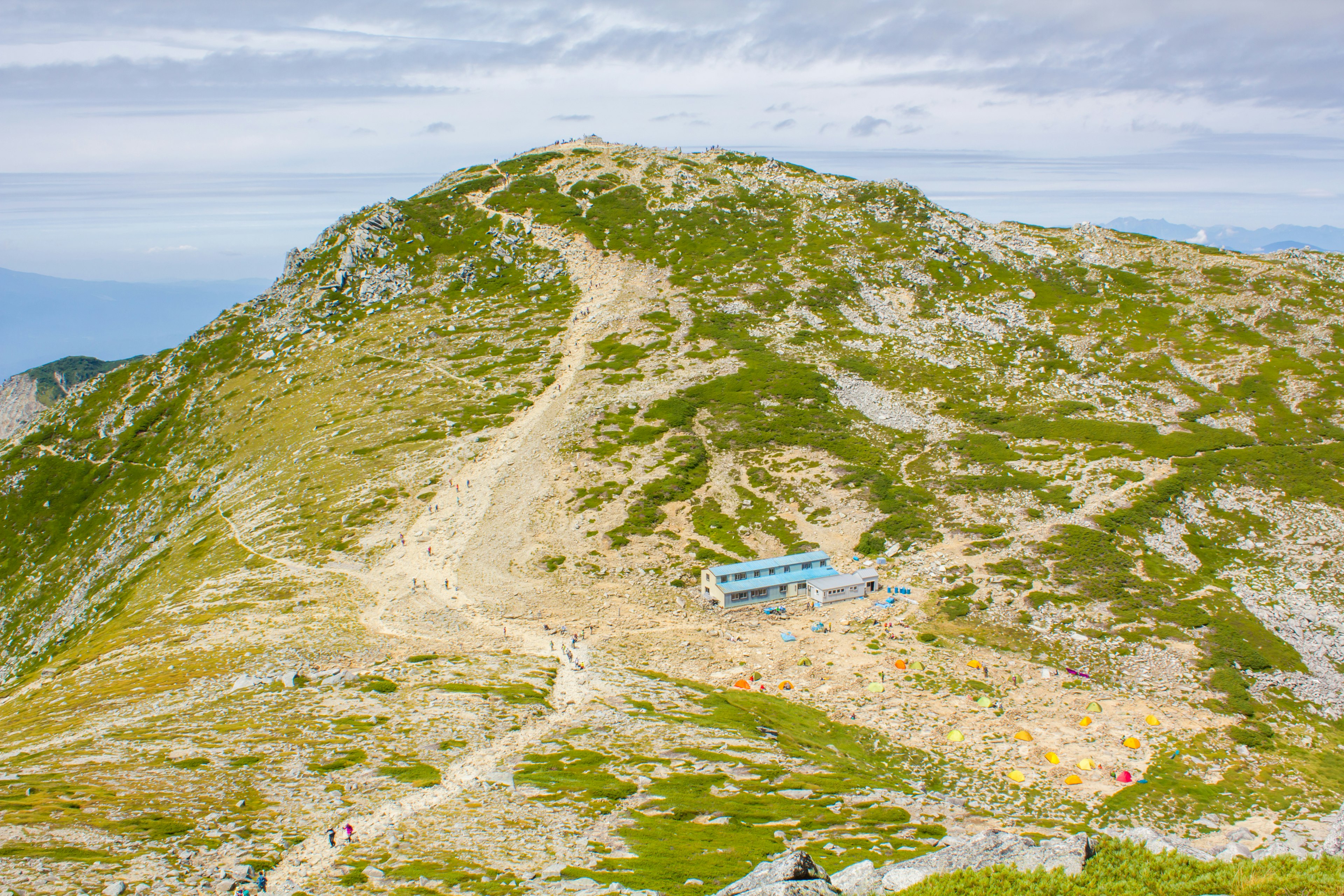 Vue panoramique d'un sommet de montagne avec des prairies vertes et un petit bâtiment bleu