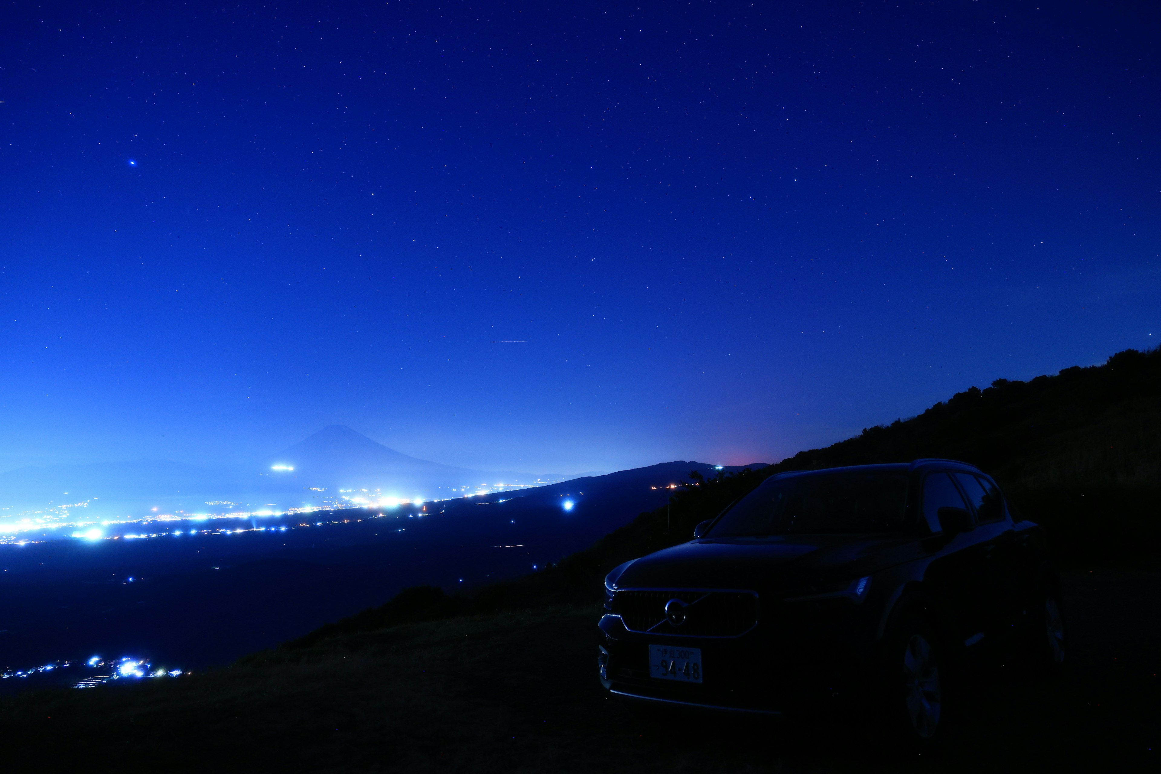 Silhouette di un'auto contro un cielo notturno stellato e belle luci cittadine