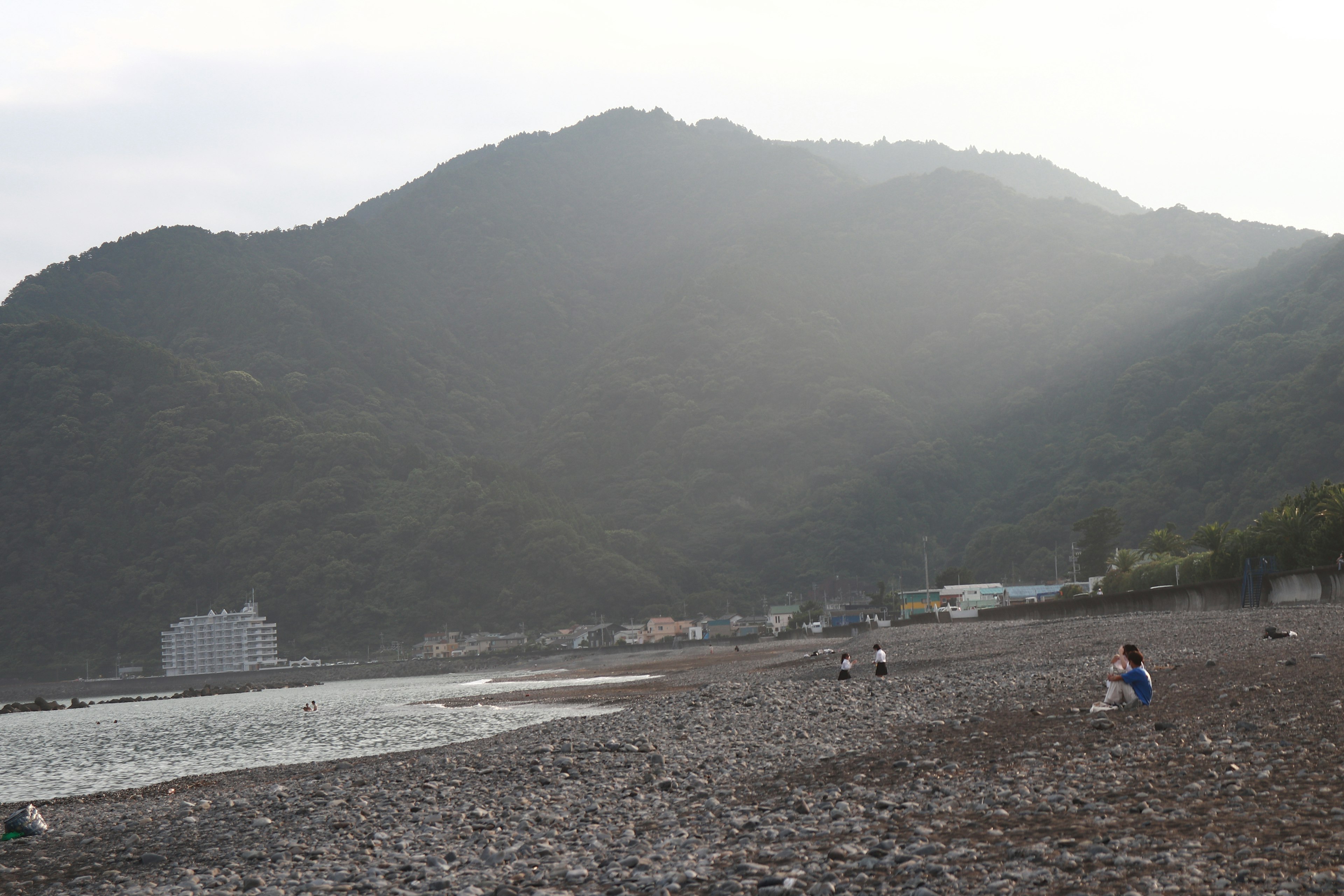 Playa de piedras con montañas al fondo y personas sentadas