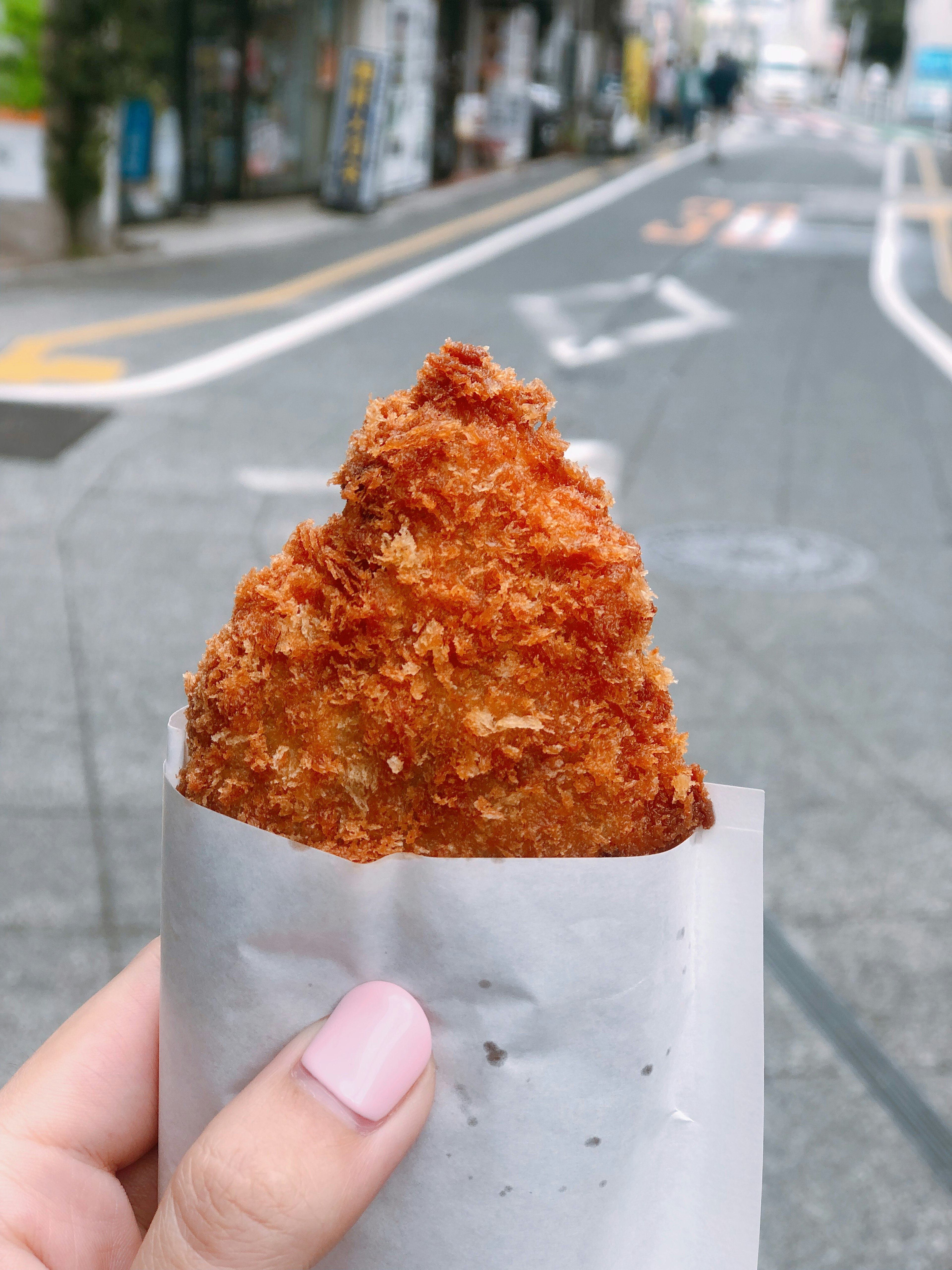 Une main tenant un croquette croustillante devant une rue de la ville