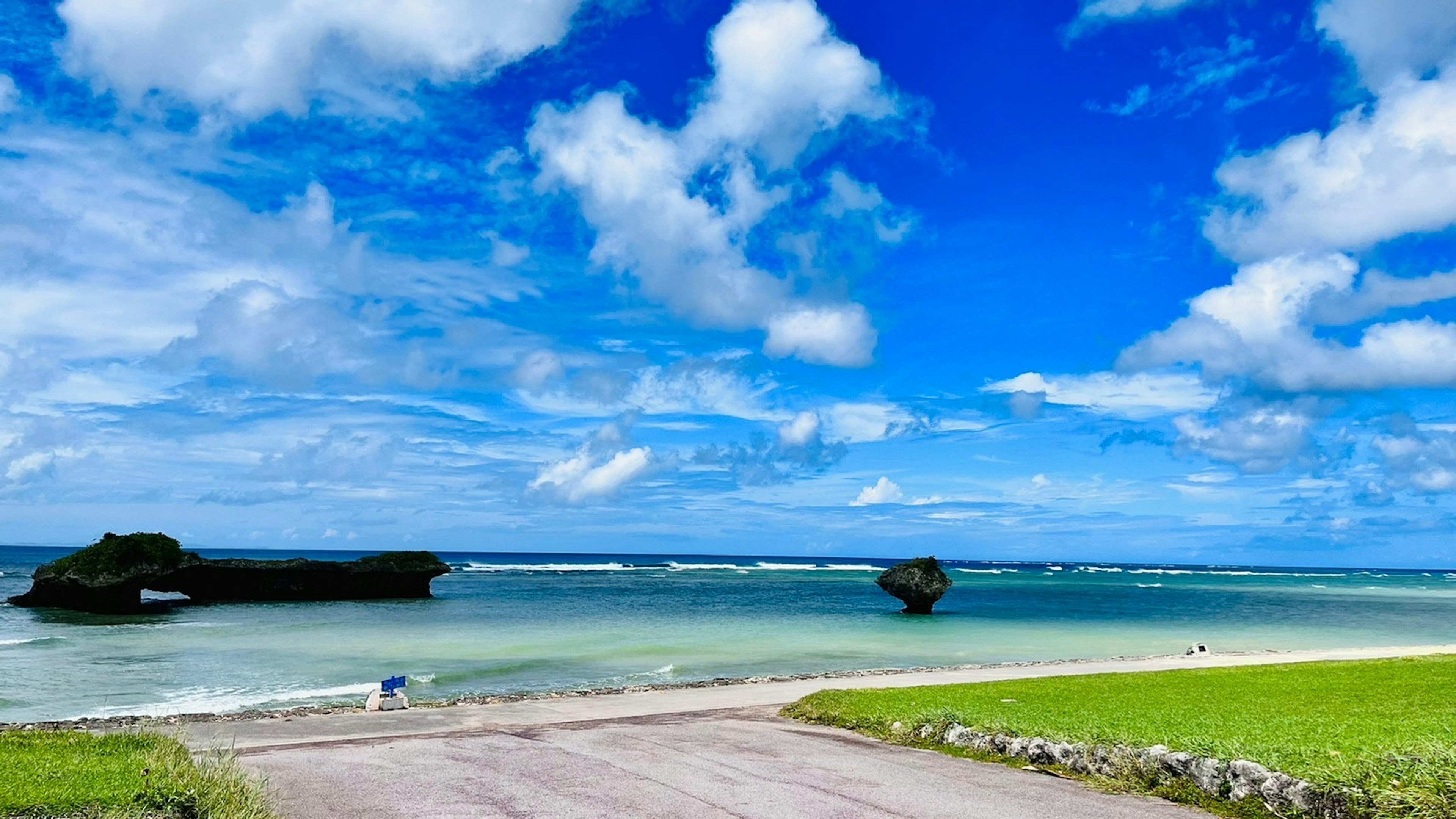 Malersicher Strandblick mit blauem Himmel und weißen Wolken grünem Gras und ruhigem Wasser