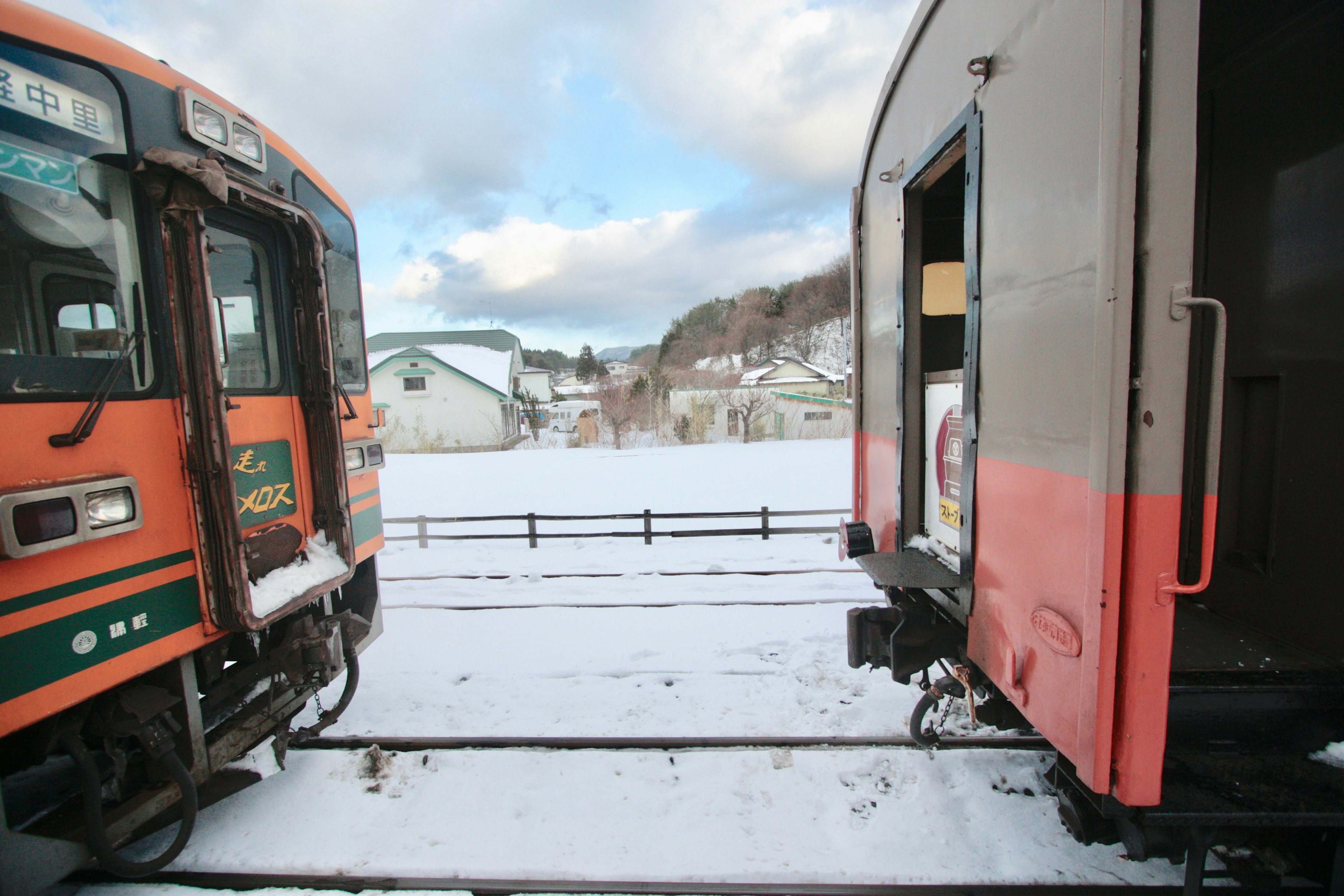 雪の中に停車している電車の車両が二つ並ぶ風景