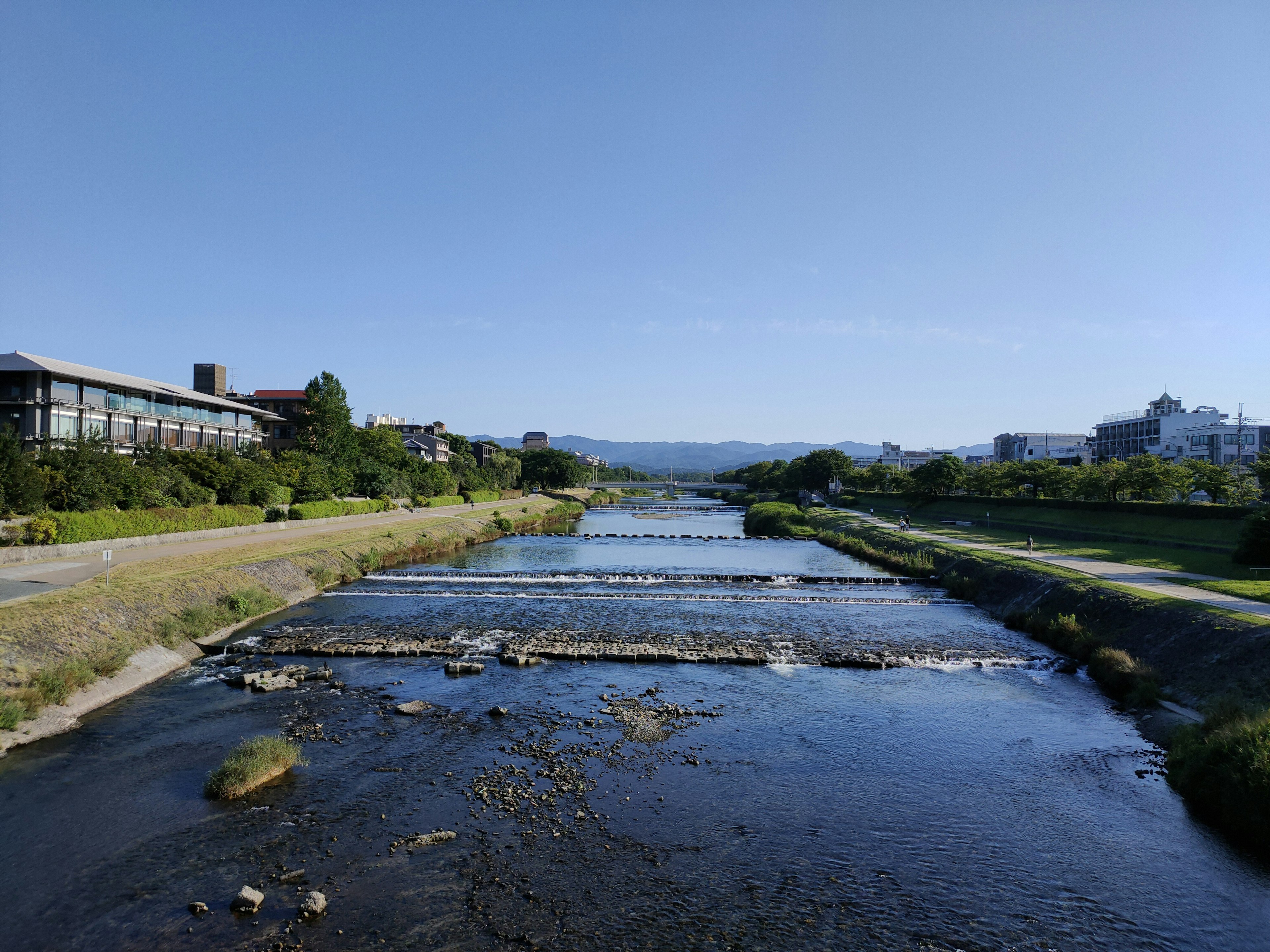 Ein Fluss, der unter einem klaren blauen Himmel fließt, mit Grün entlang des Ufers