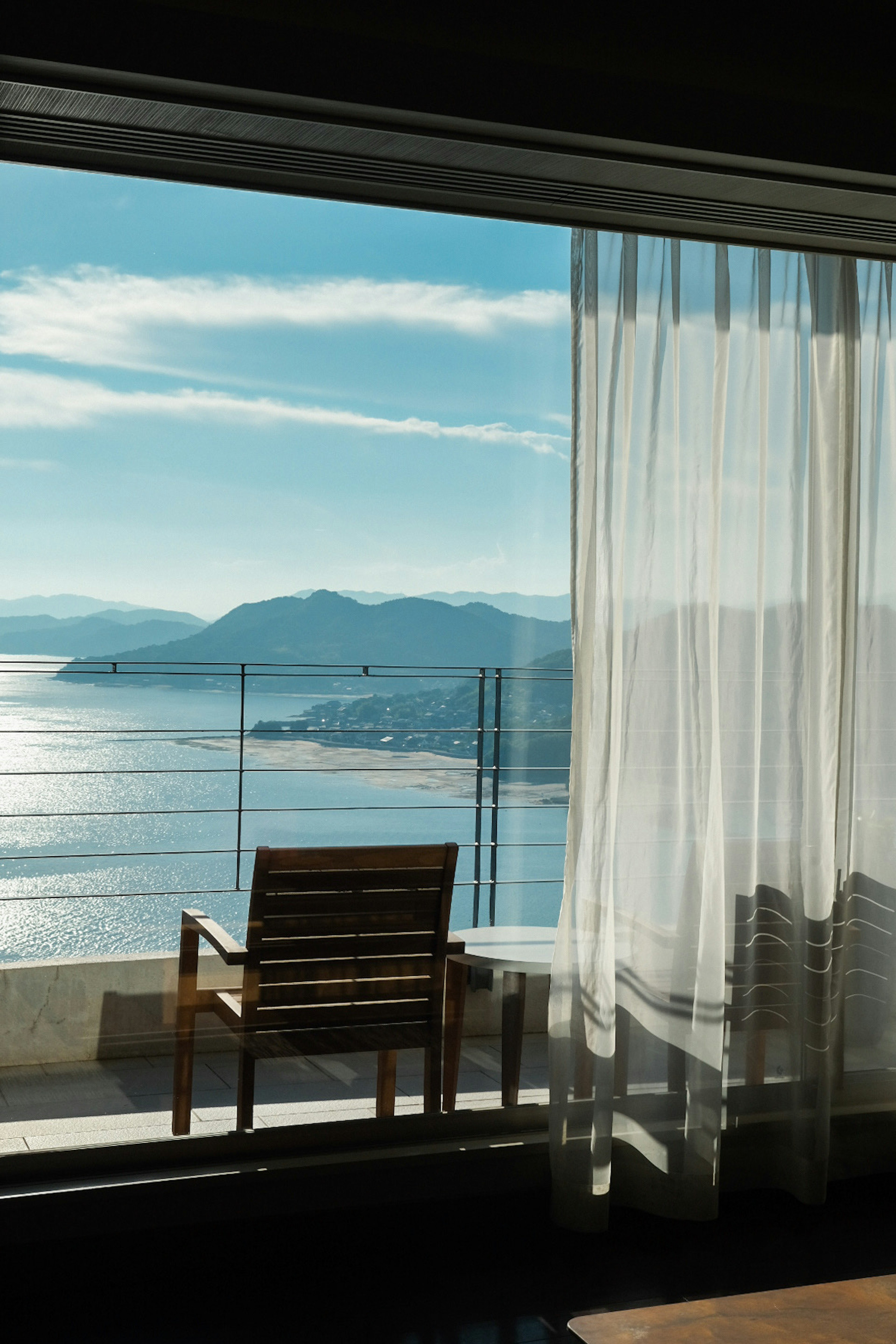 Interior view with large window showing ocean scenery and sheer white curtains