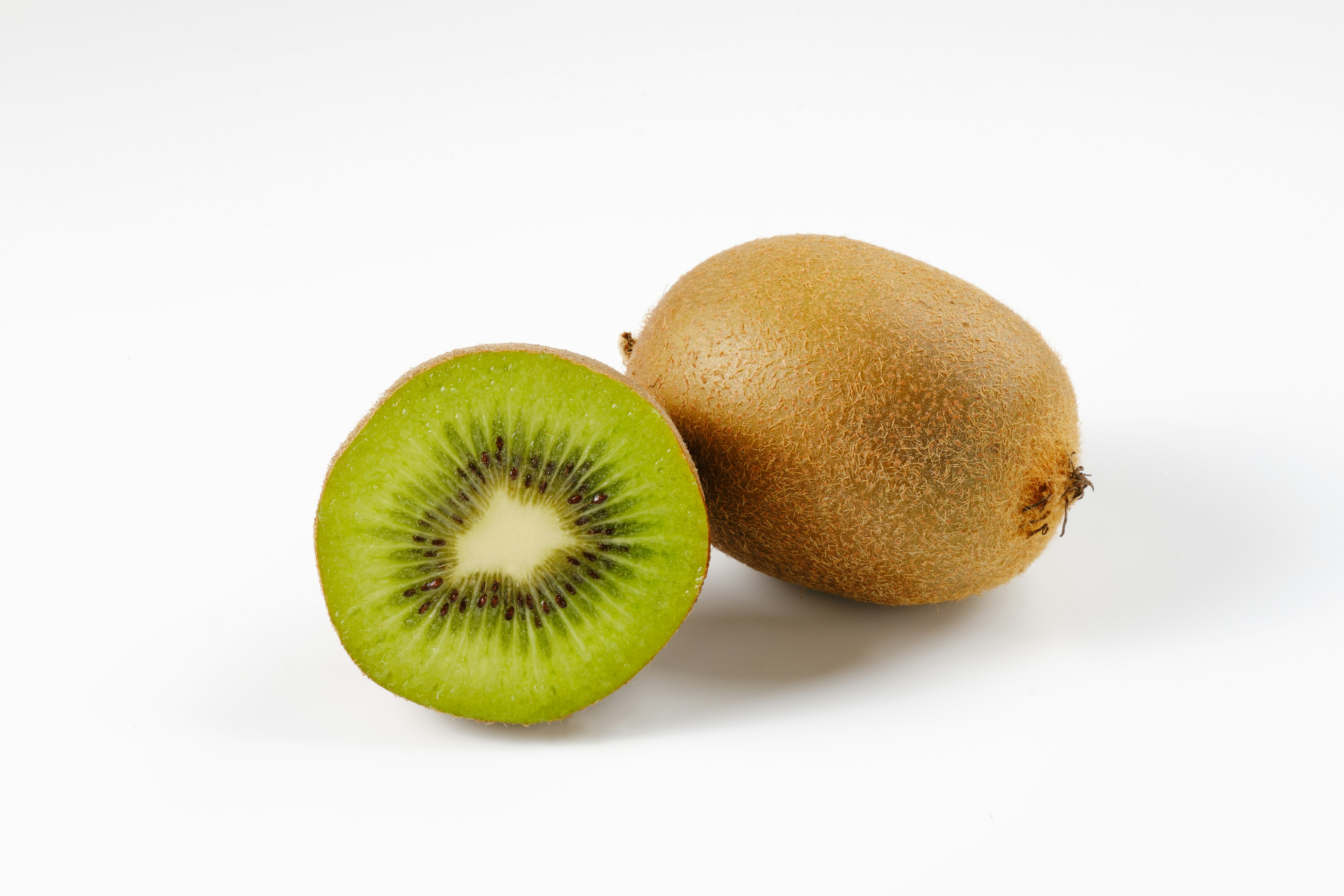 Một quả kiwi nguyên và một quả kiwi đã cắt cho thấy phần thịt màu xanh trên nền trắng