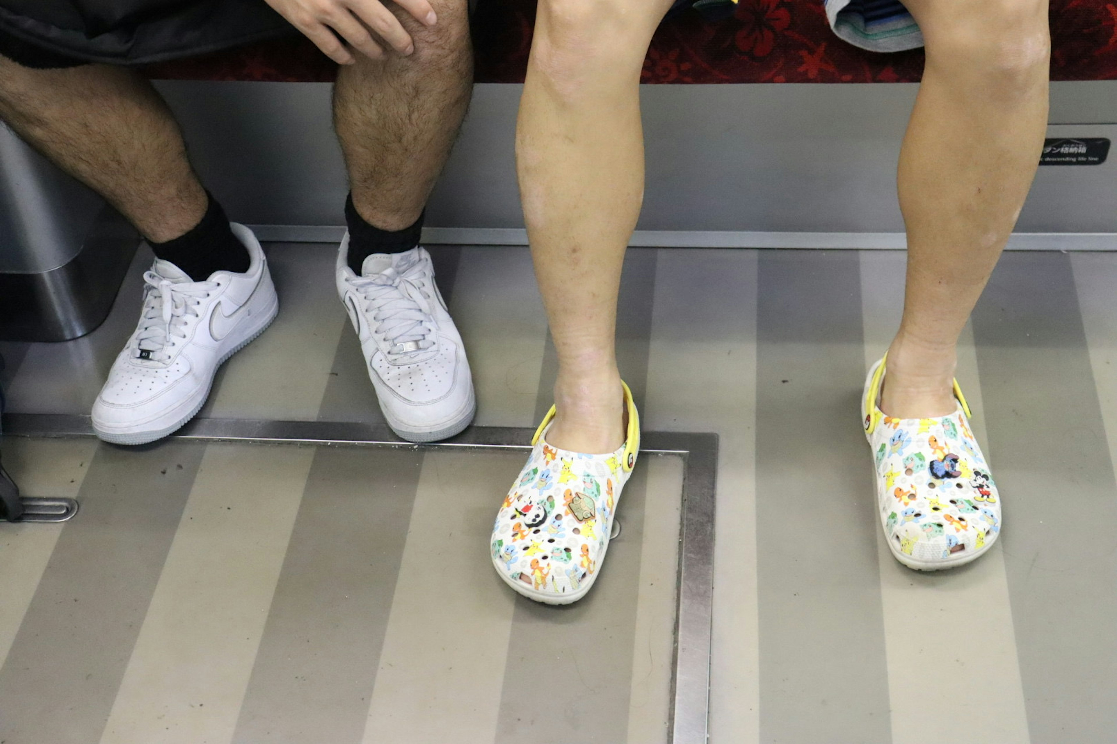 A colorful clog-wearing foot next to a white sneaker-wearing foot on a subway