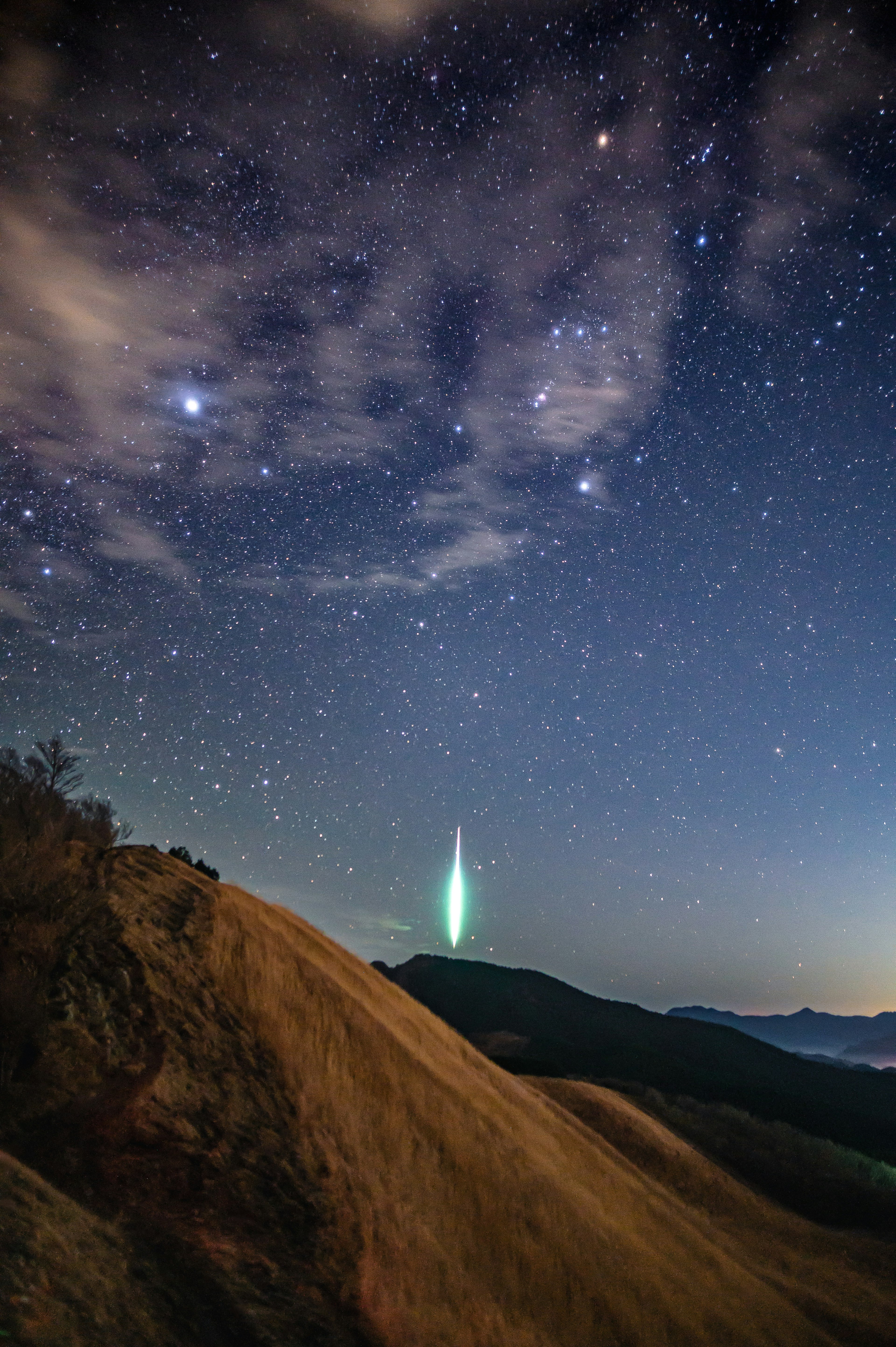 Ein leuchtendes grünes Licht unter einem sternenklaren Himmel mit Bergsilhouetten