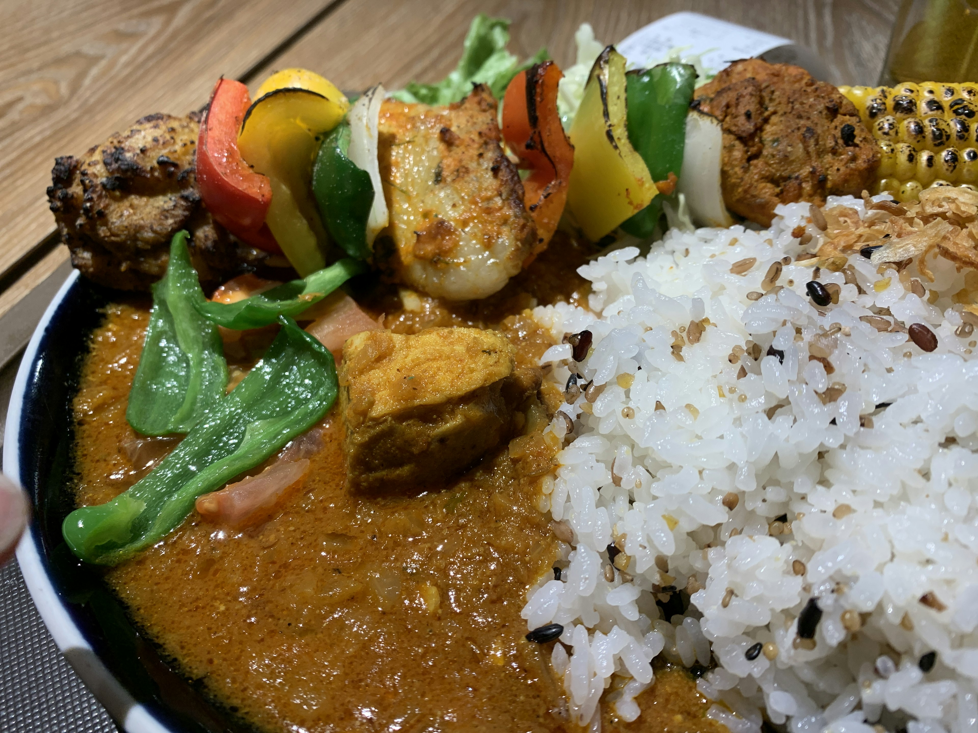 A vibrant plate of curry with rice accompanied by colorful skewered vegetables and meat