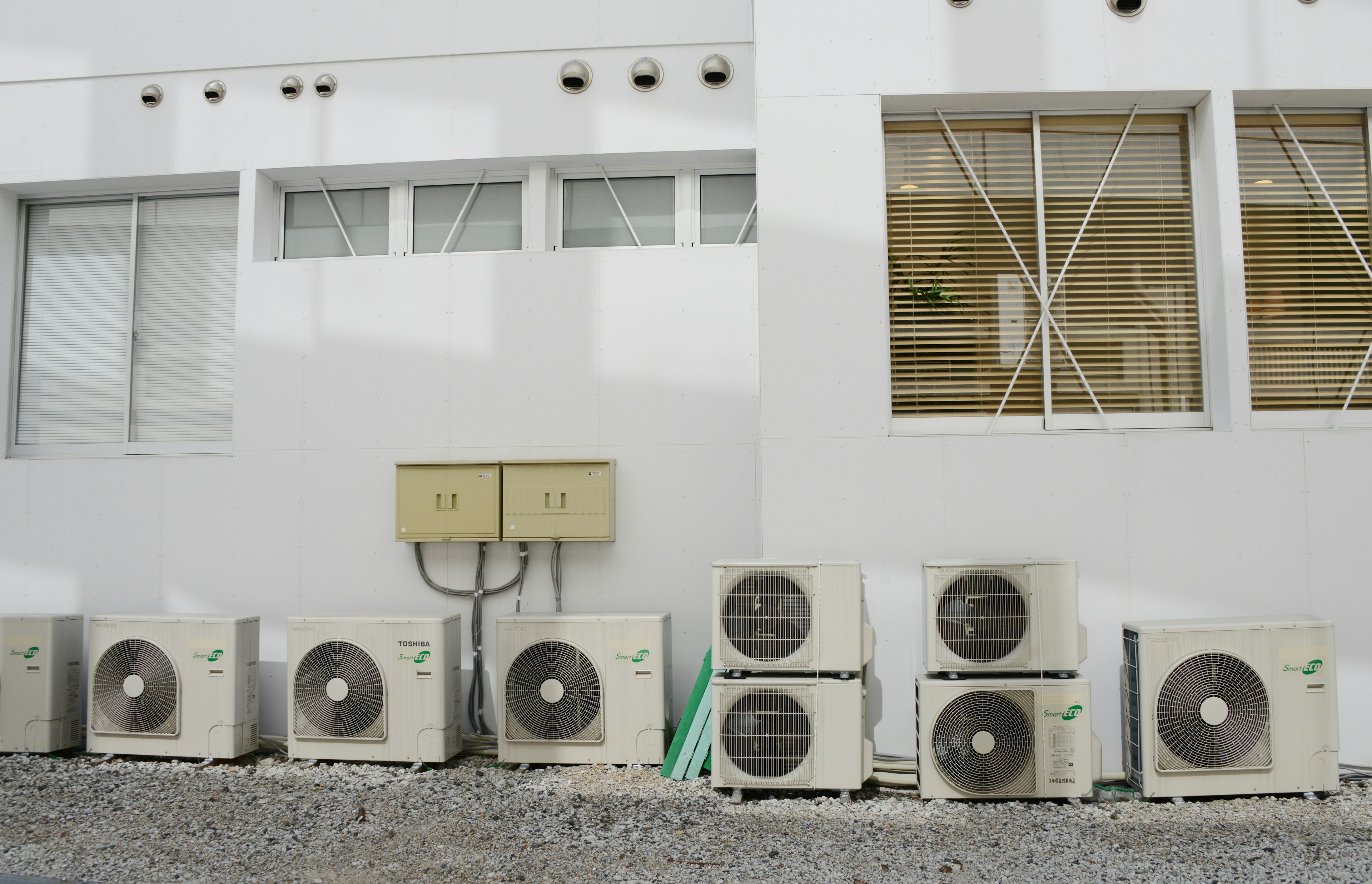 Multiple air conditioning units attached to a white wall with a window