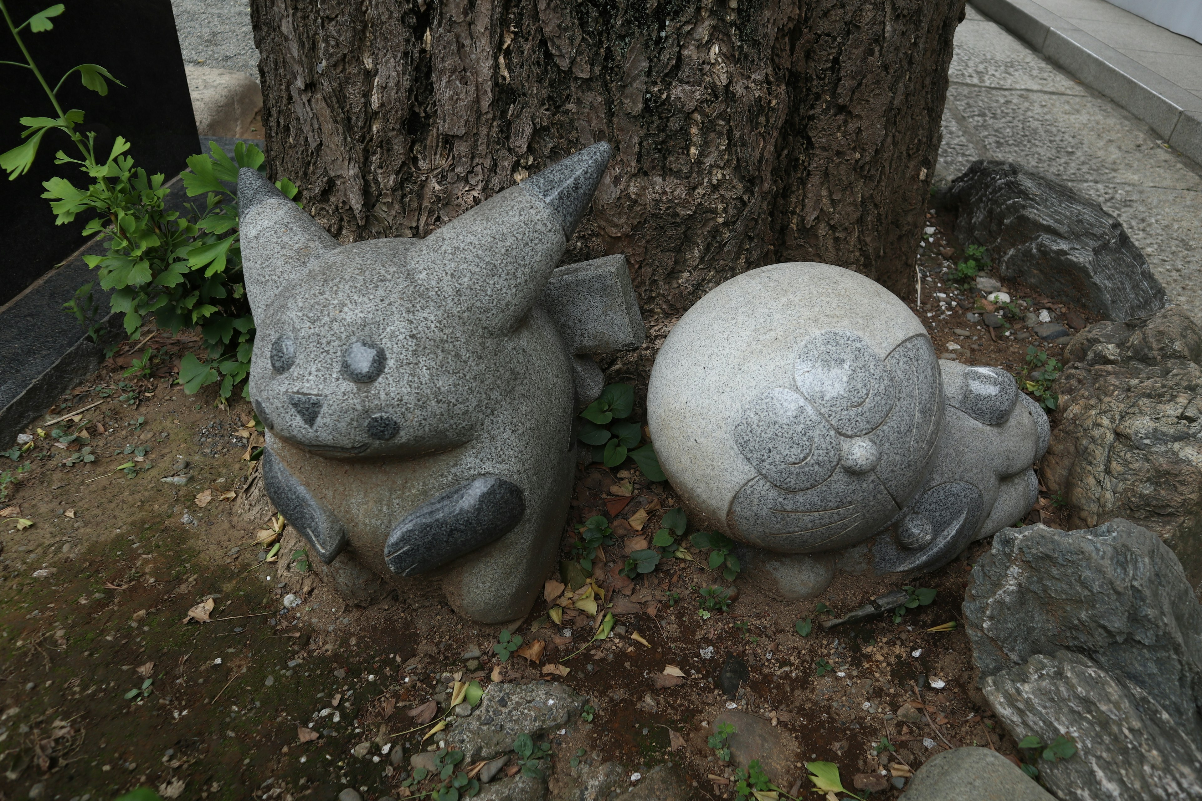 Estatuas de Pokémon de piedra gris al lado de un árbol