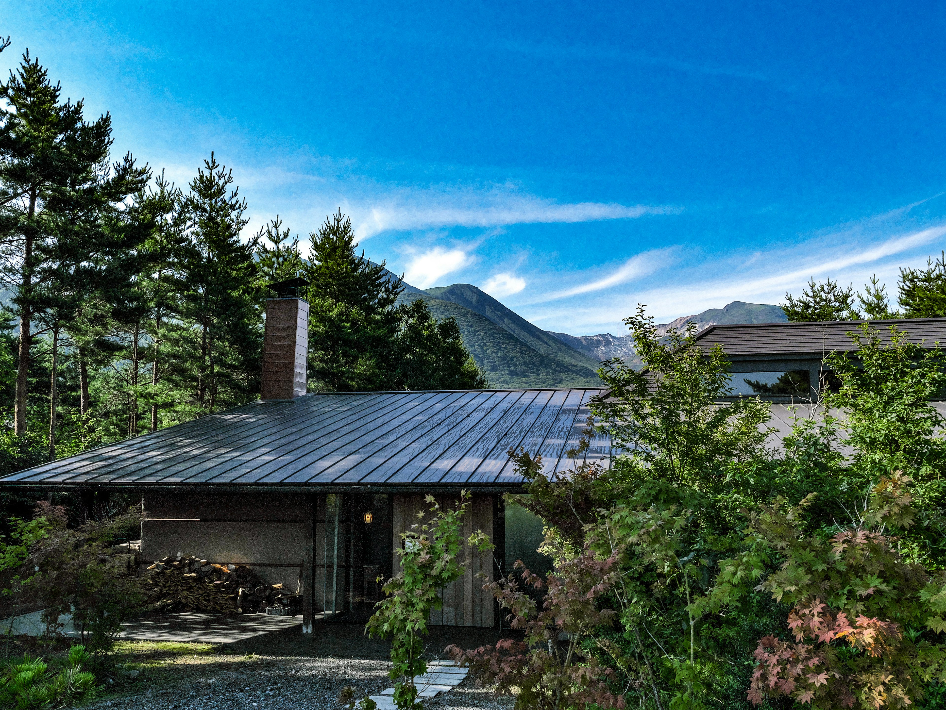 Modernes Haus umgeben von üppigem Grün mit Bergen und blauem Himmel im Hintergrund