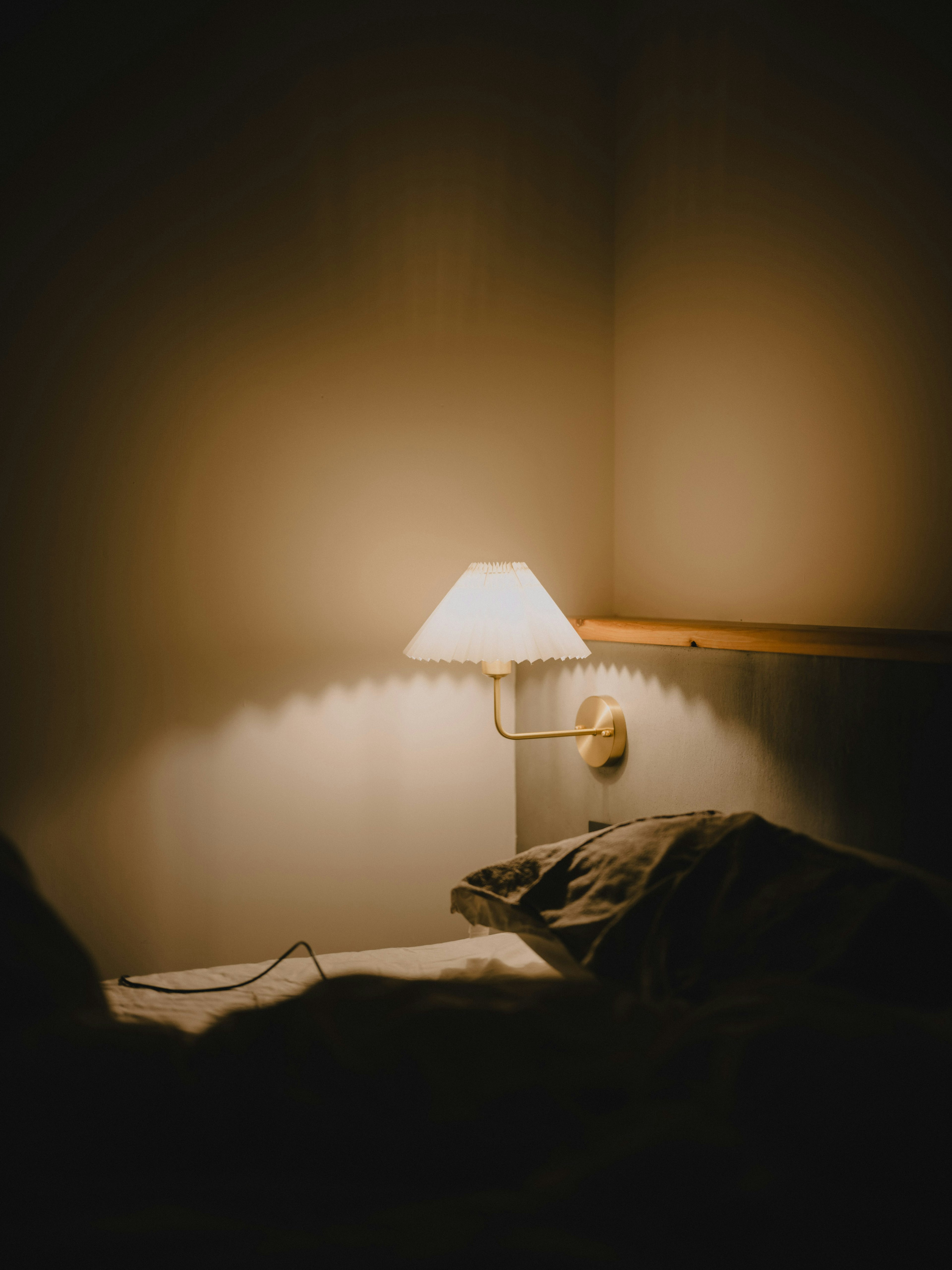 A cozy corner of a room featuring a soft-lit lamp and part of a bed