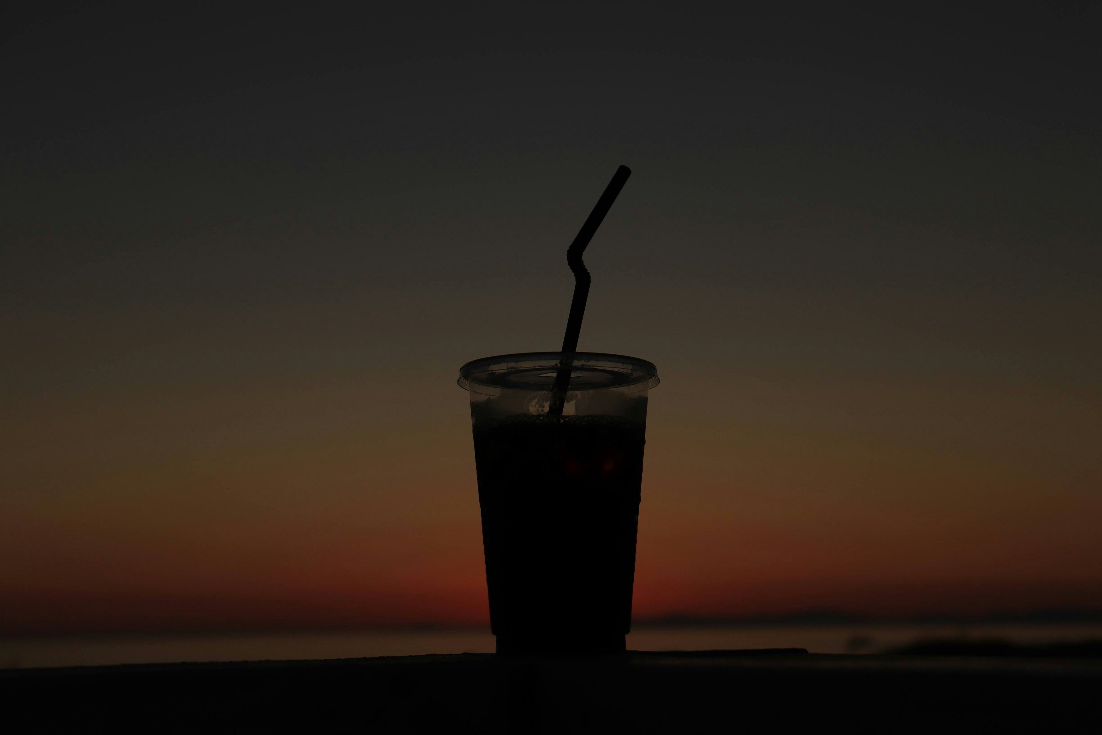 夕暮れ時のシルエットの飲み物とストロー