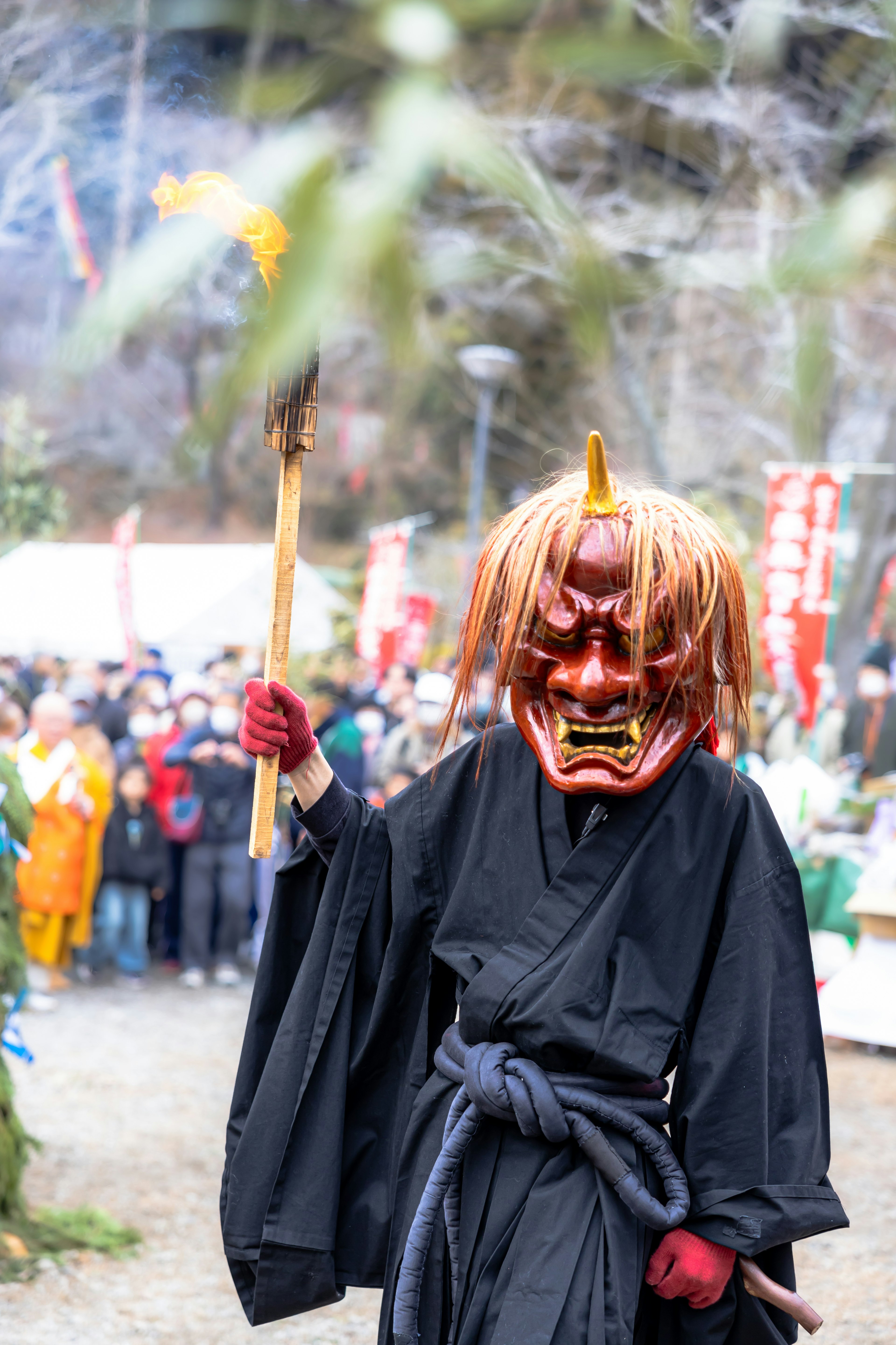 Eine Figur mit einer roten Dämonenmaske in traditioneller schwarzer Kleidung auf einem Festival