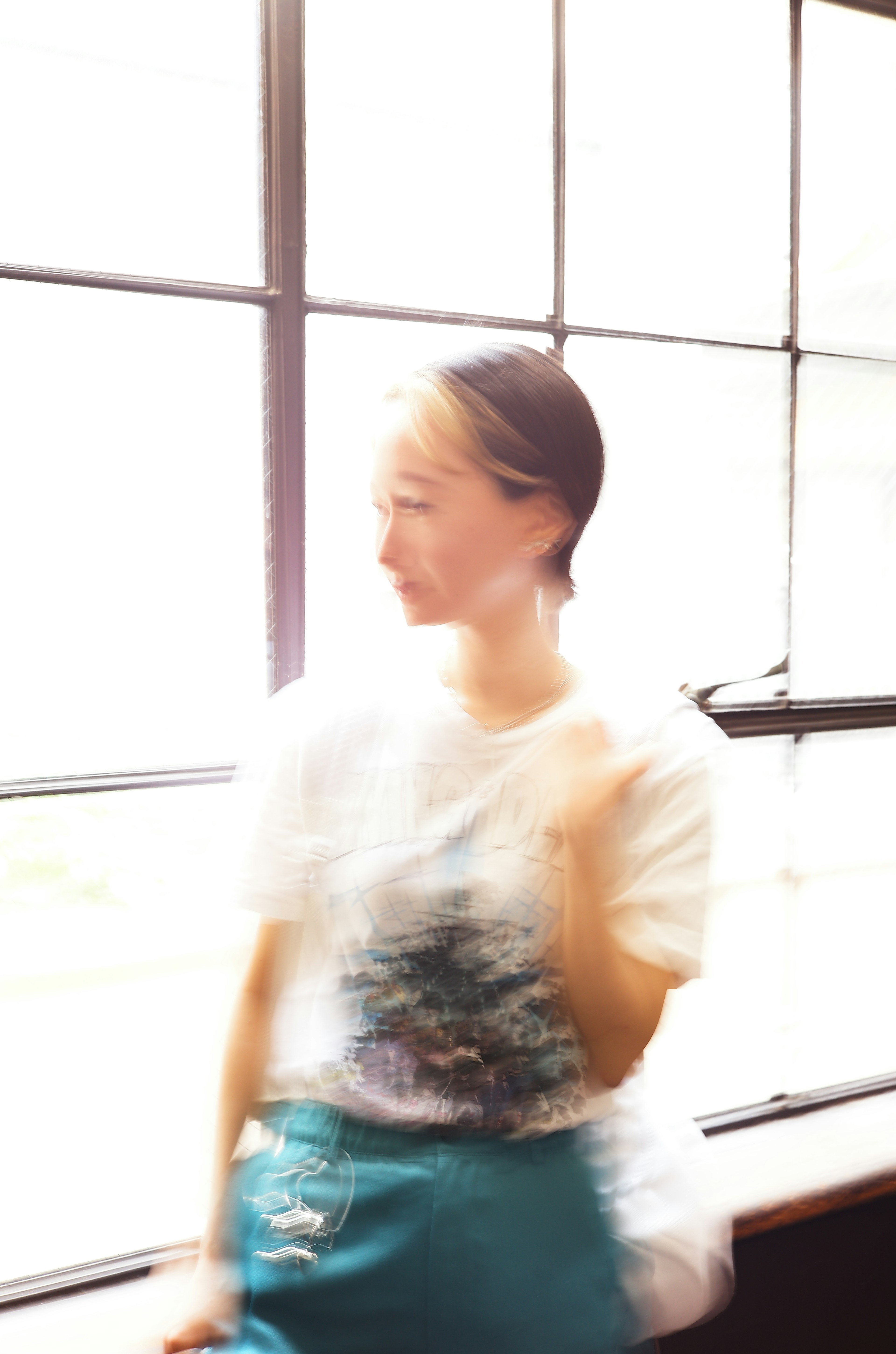 Image floue d'une femme debout près d'une fenêtre portant un t-shirt blanc et une jupe bleue avec un éclairage doux