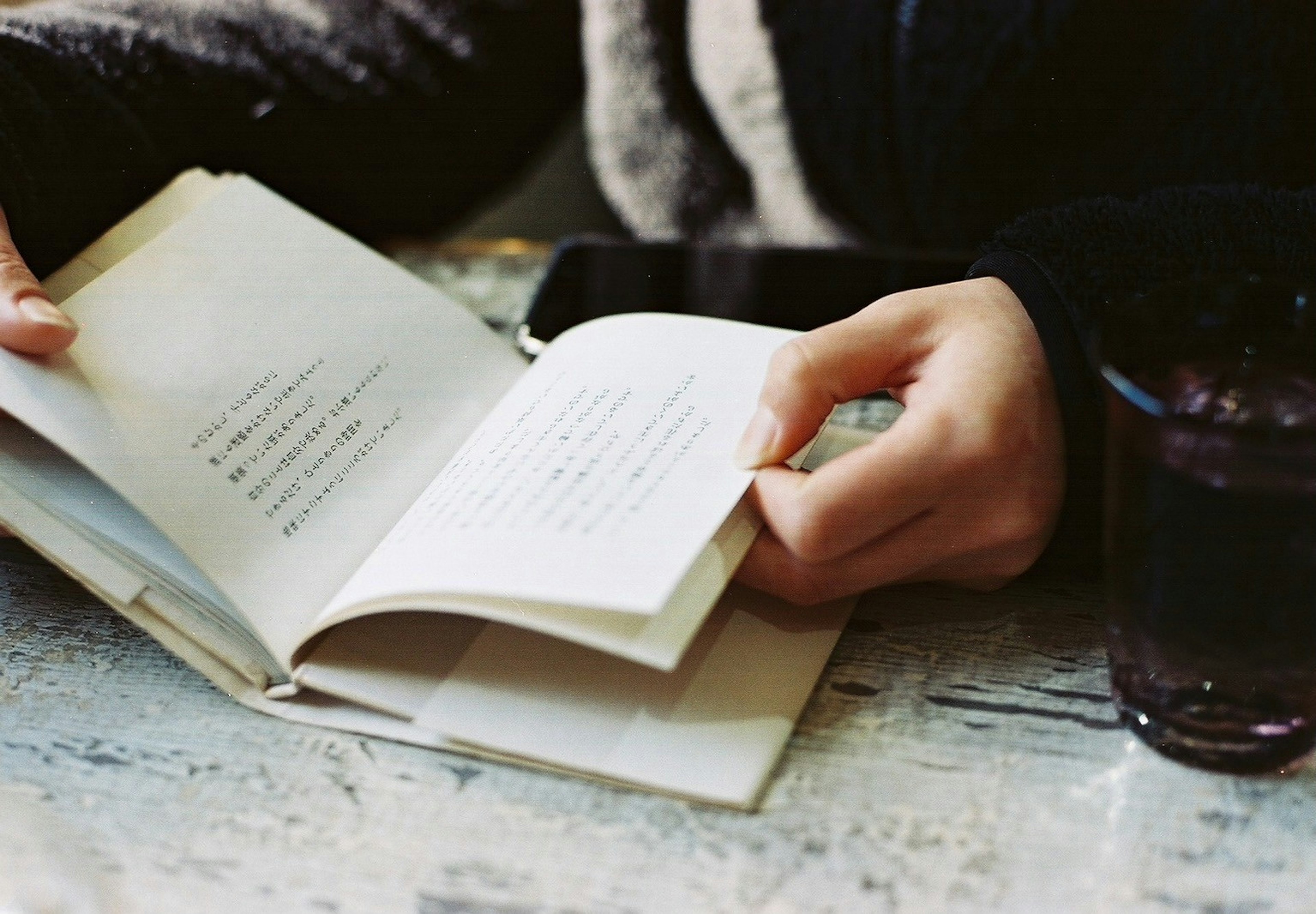 Hand holding a book with a drink on a table