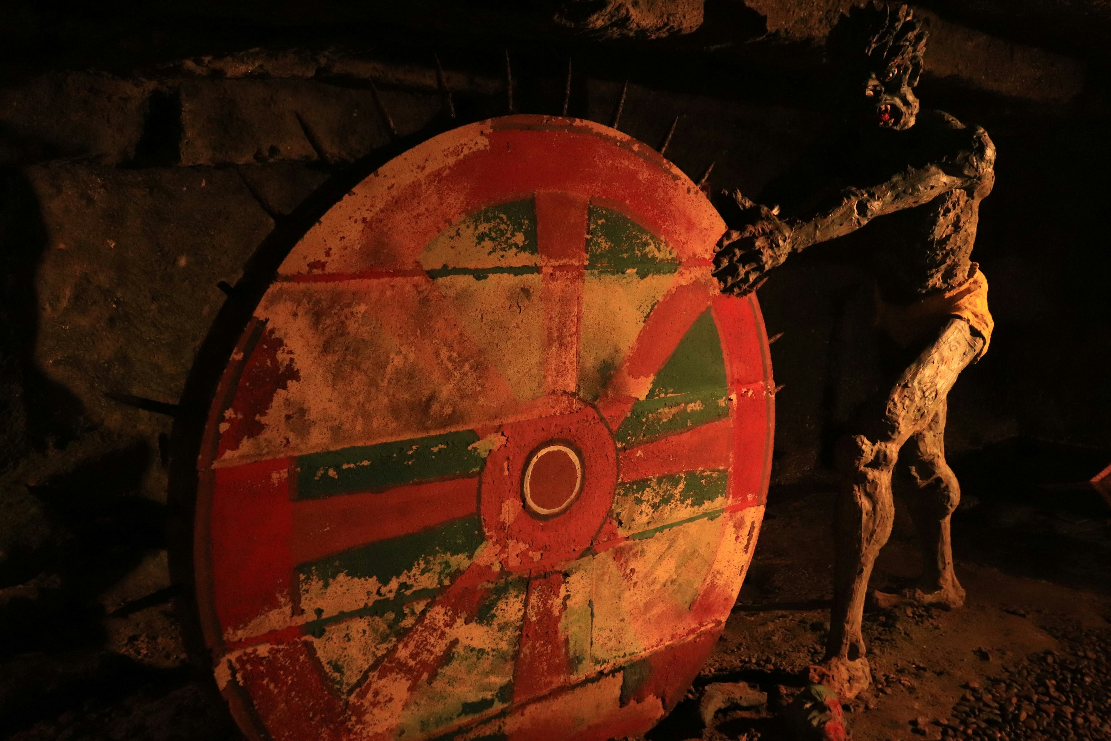 An ancient wooden shield with colorful designs beside a sculpted figure in a dimly lit space