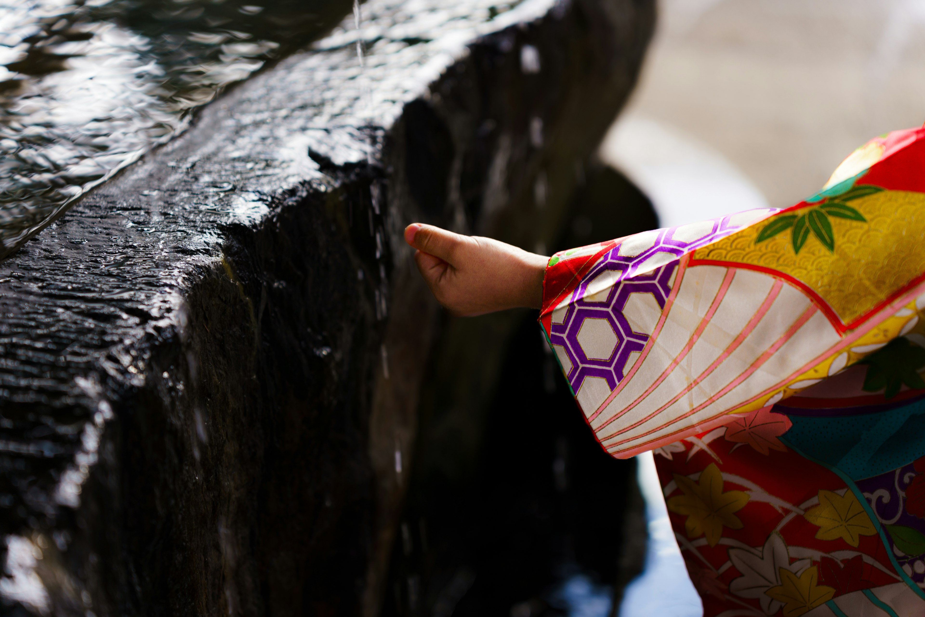 Kind im bunten Kimono, das die Hand nach fließendem Wasser ausstreckt