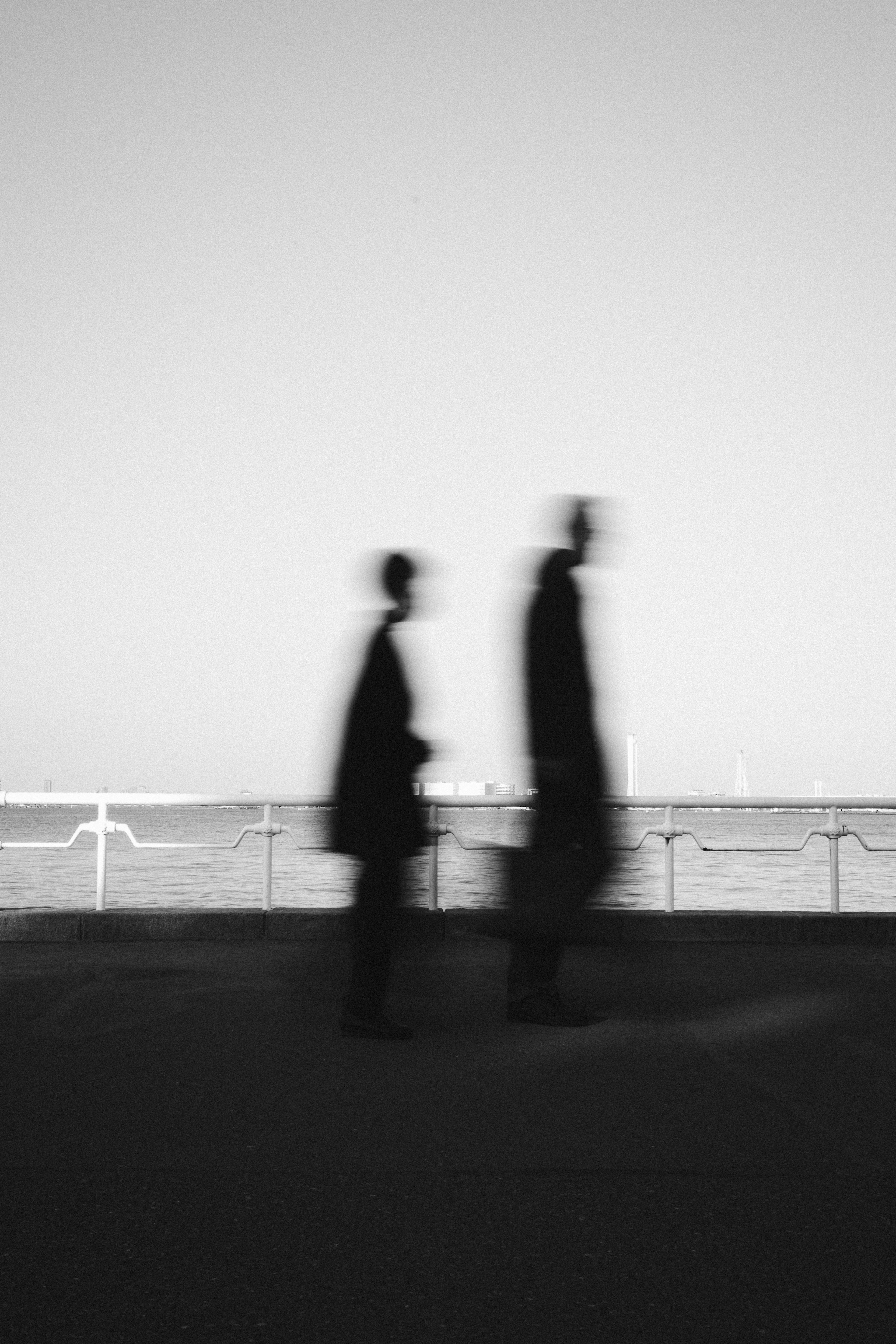 Silhouetten von Personen, die am Meer entlang gehen in einem Schwarz-Weiß-Foto