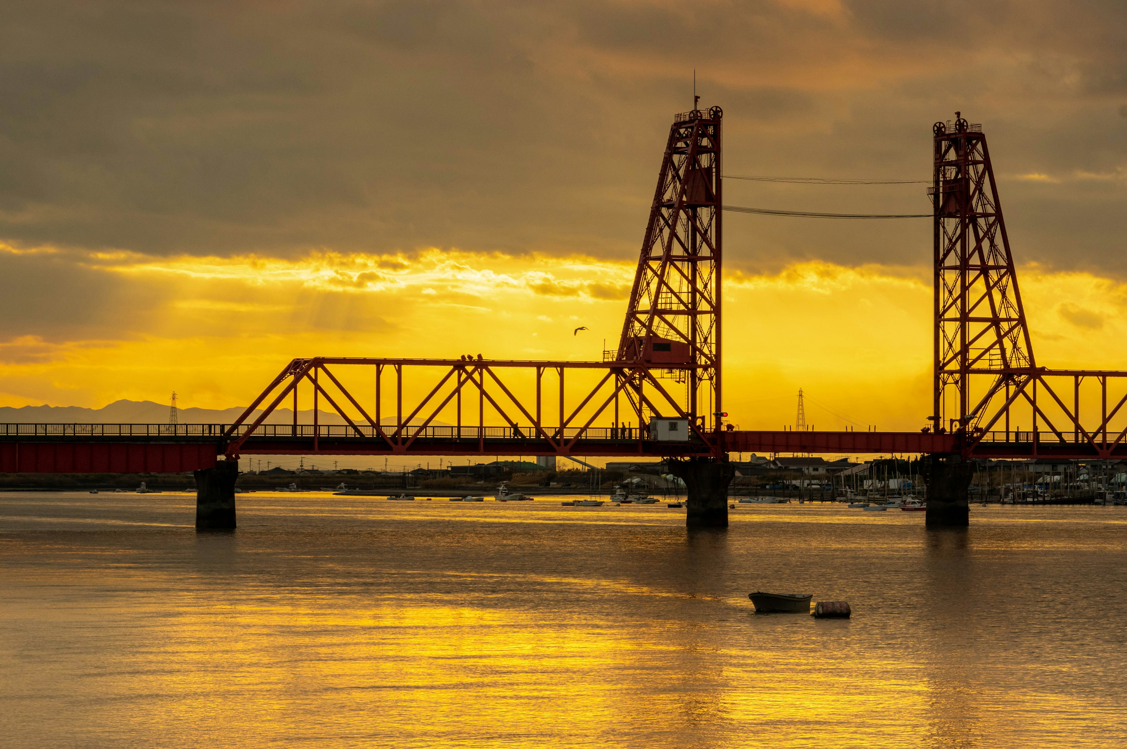 Red bridge silhouetted against a sunset with calm waters