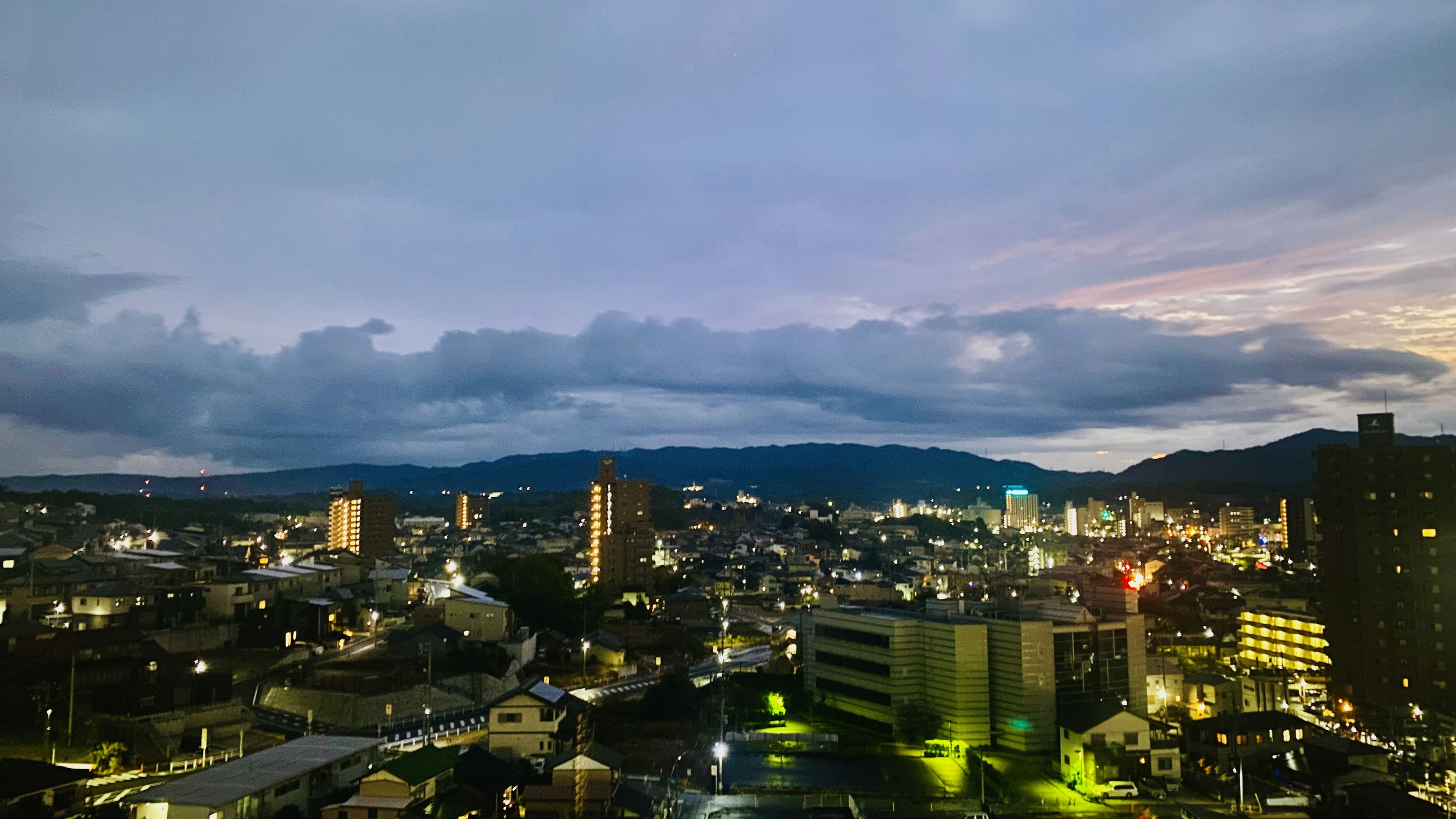 Vue de la ville au crépuscule avec des immeubles et des maisons éclairés par des lampadaires sous un ciel nuageux