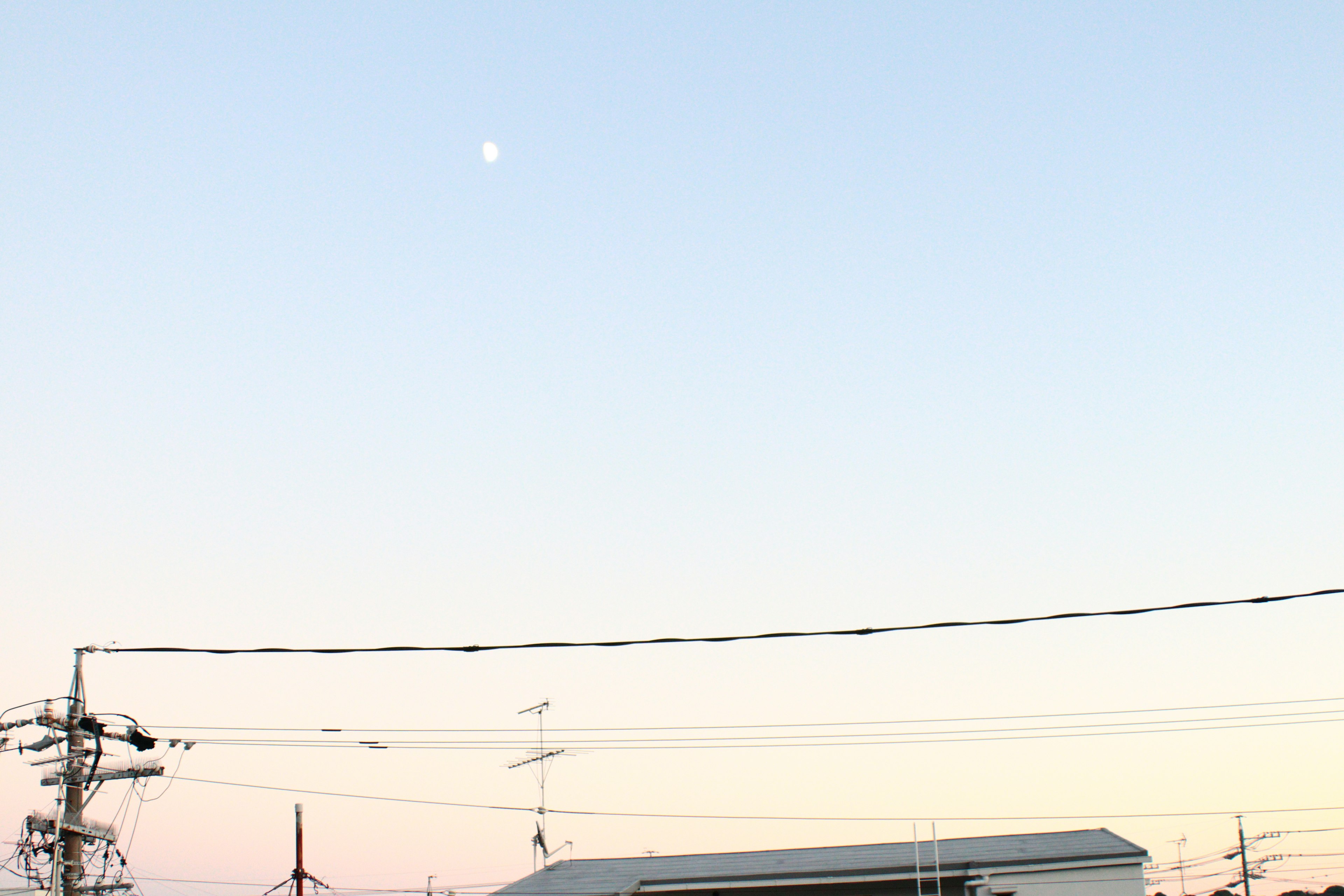 A landscape featuring the moon in a light sky with power lines