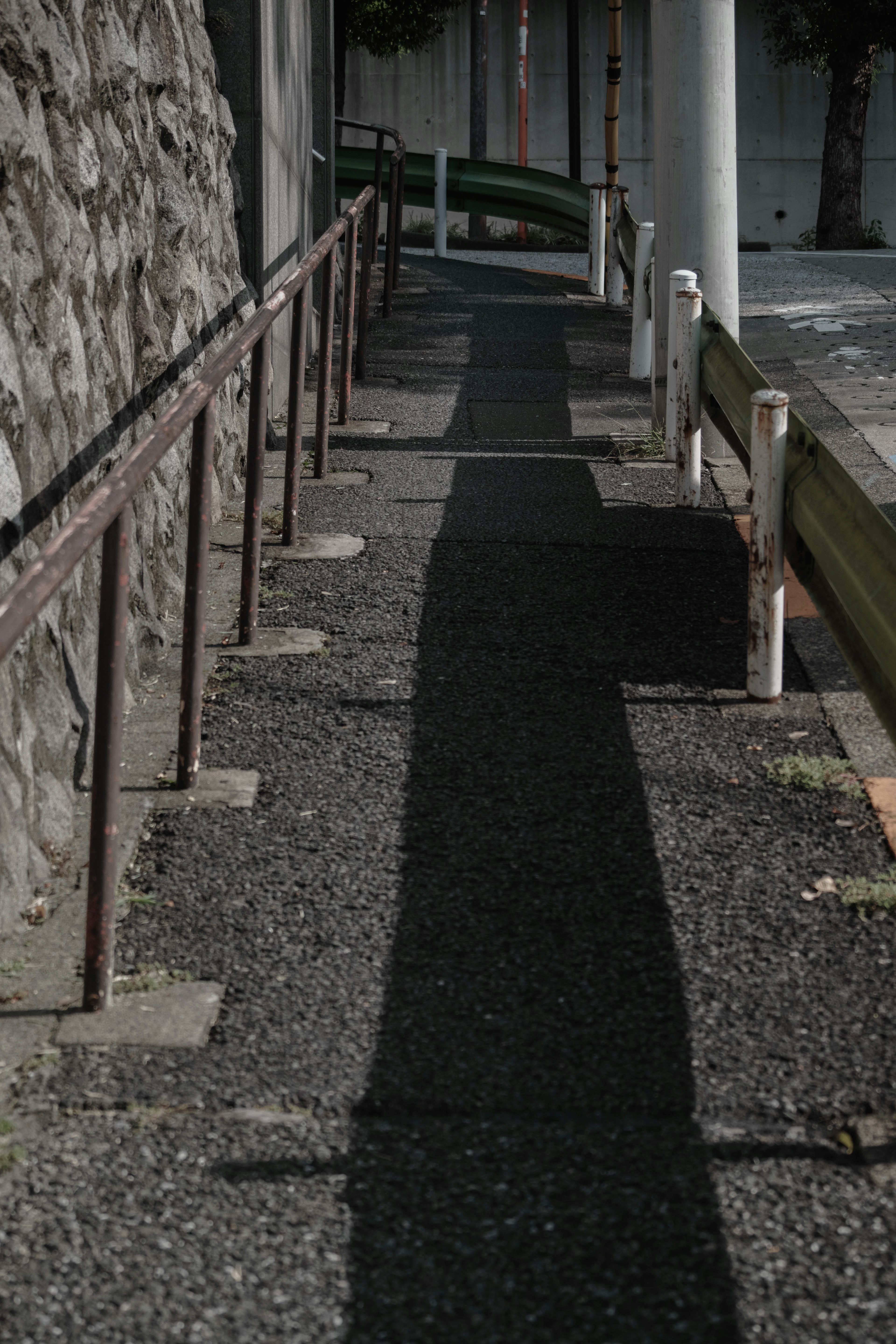 Sidewalk with a metal railing and shadow alongside a stone wall