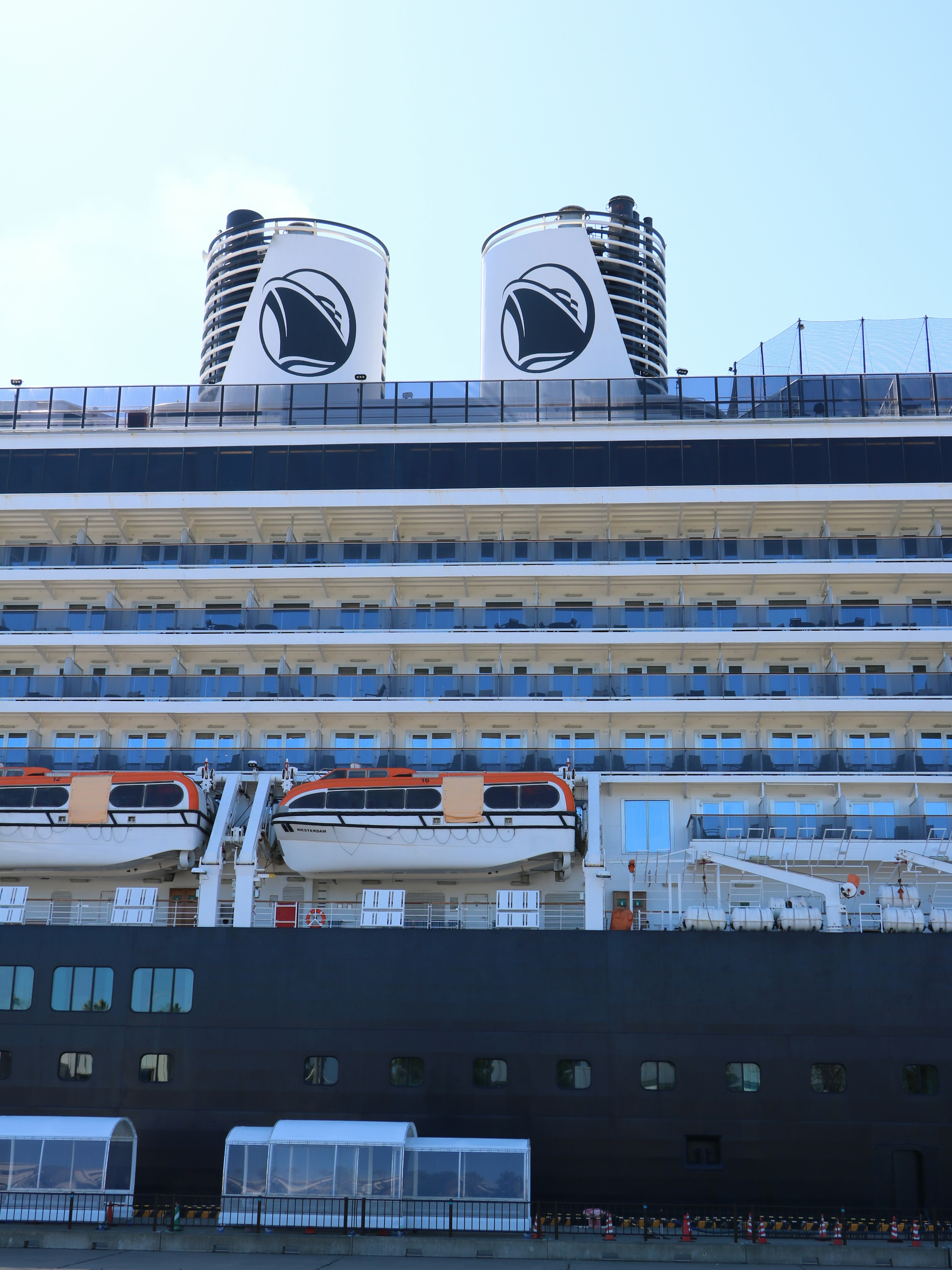 Seitenansicht eines Kreuzfahrtschiffes mit weißen und schwarzen Streifen markanten Schornsteinen und sichtbaren Rettungsbooten