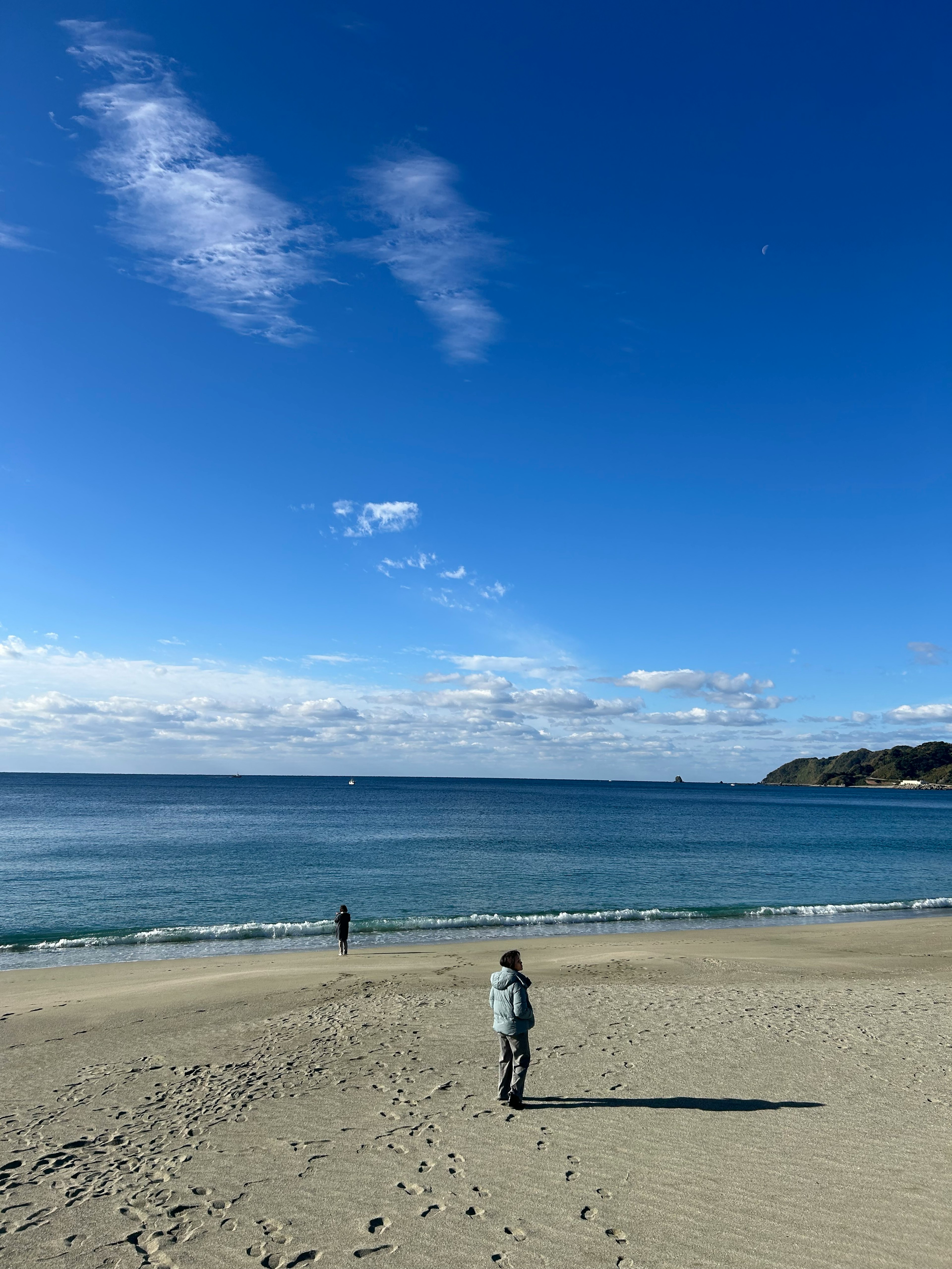 Une personne debout sur une plage sous un ciel bleu et une mer calme