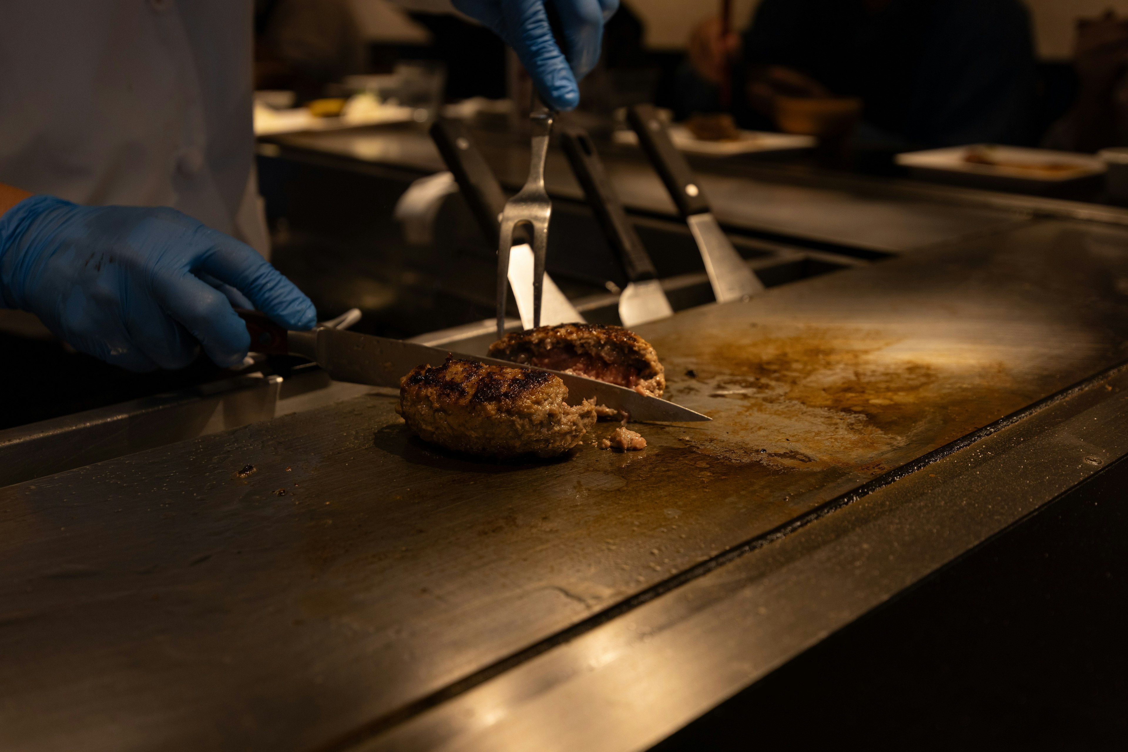 Koch mit blauen Handschuhen, der Fleisch auf einem Grill schneidet