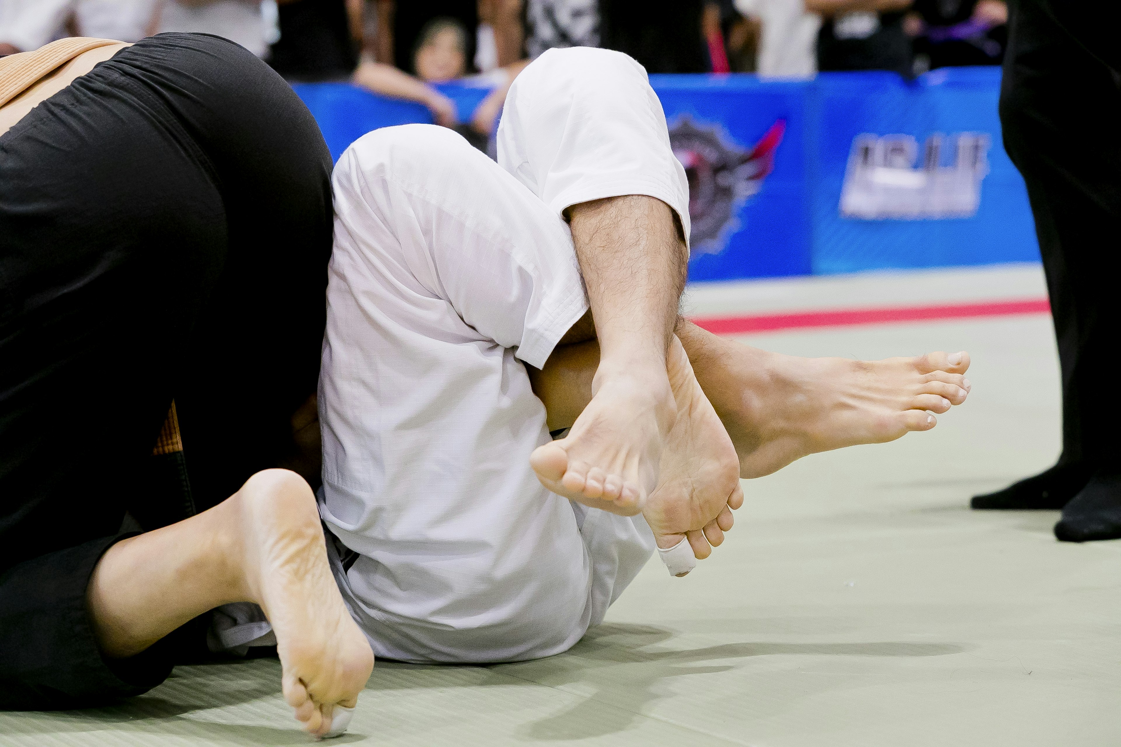 Two jiu-jitsu competitors grappling with feet prominently displayed