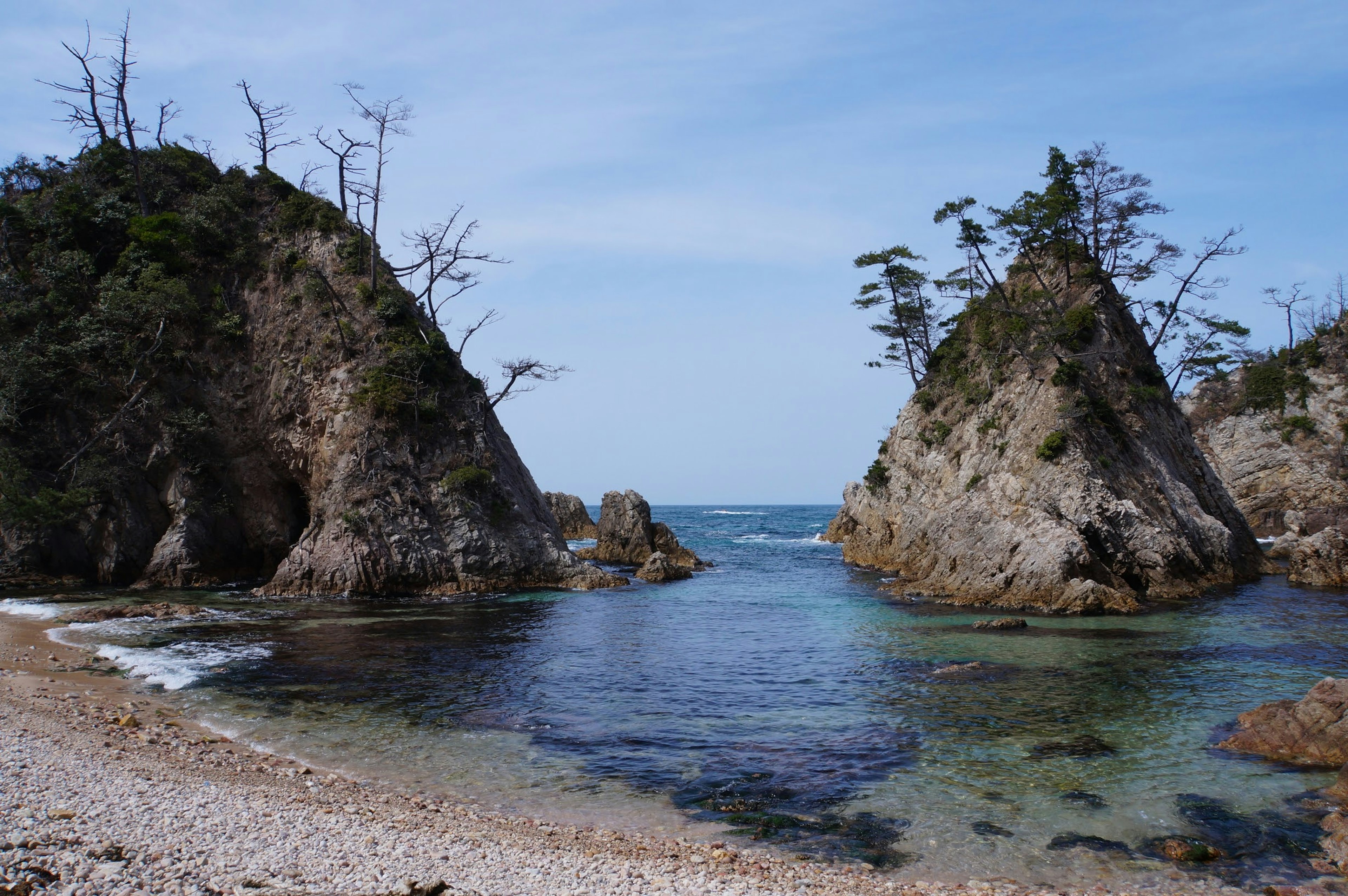 Two rocky formations surrounded by blue water and a gentle sandy beach