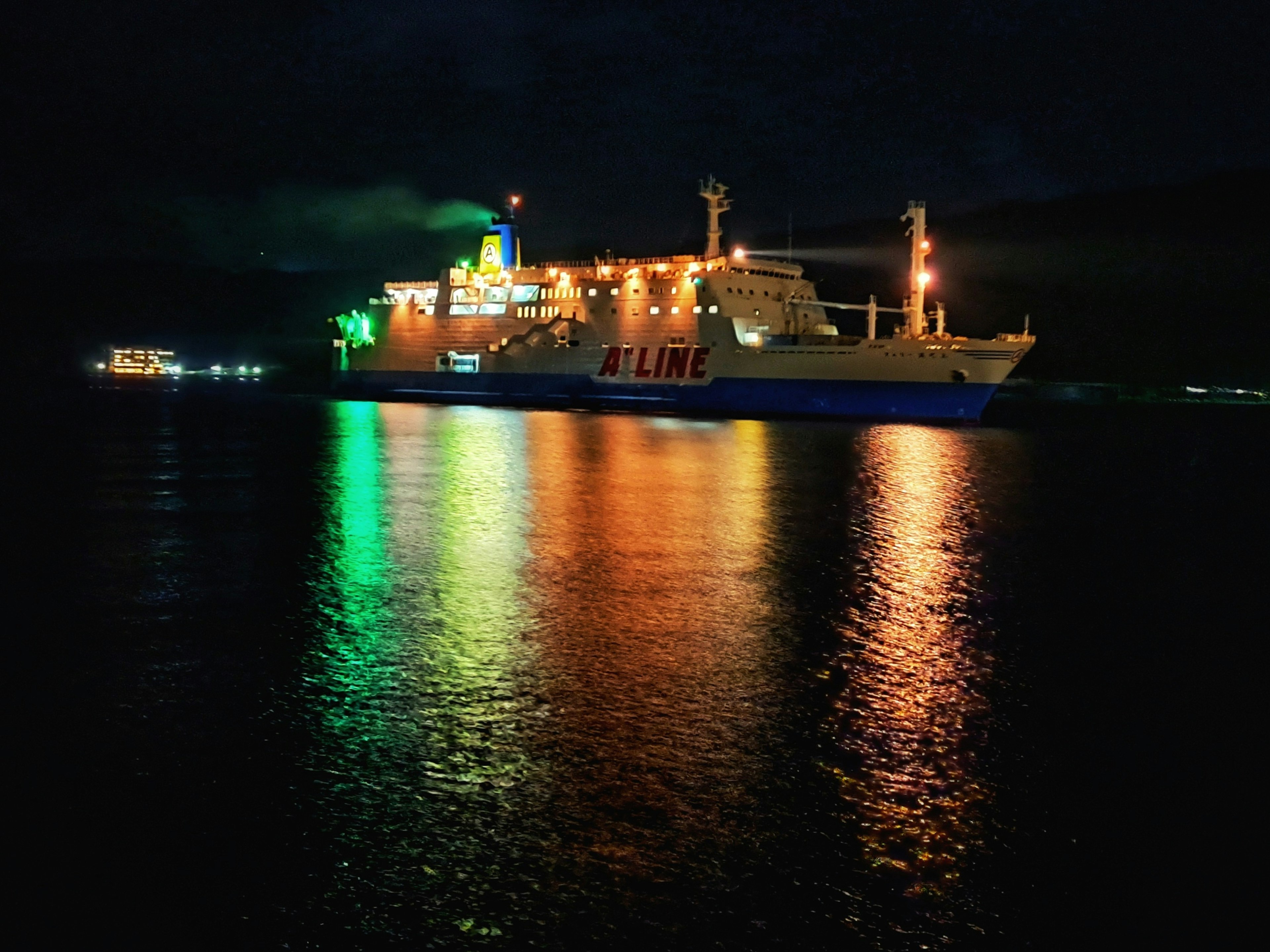 Bunt erleuchtetes Schiff in der Nacht spiegelt sich im Wasser