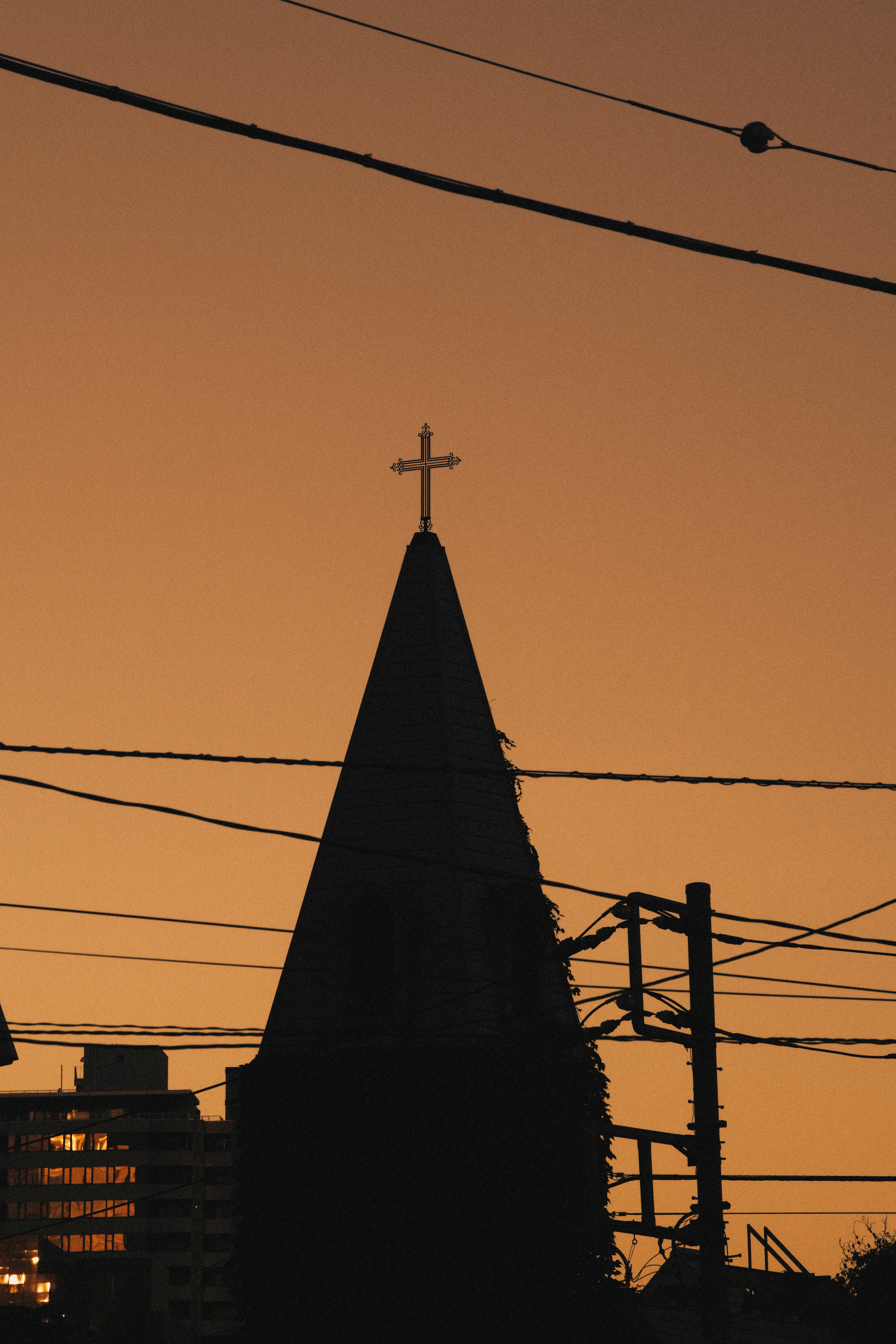 Silhouette eines Kirchturms mit einem Kreuz vor einem Sonnenuntergangshimmel