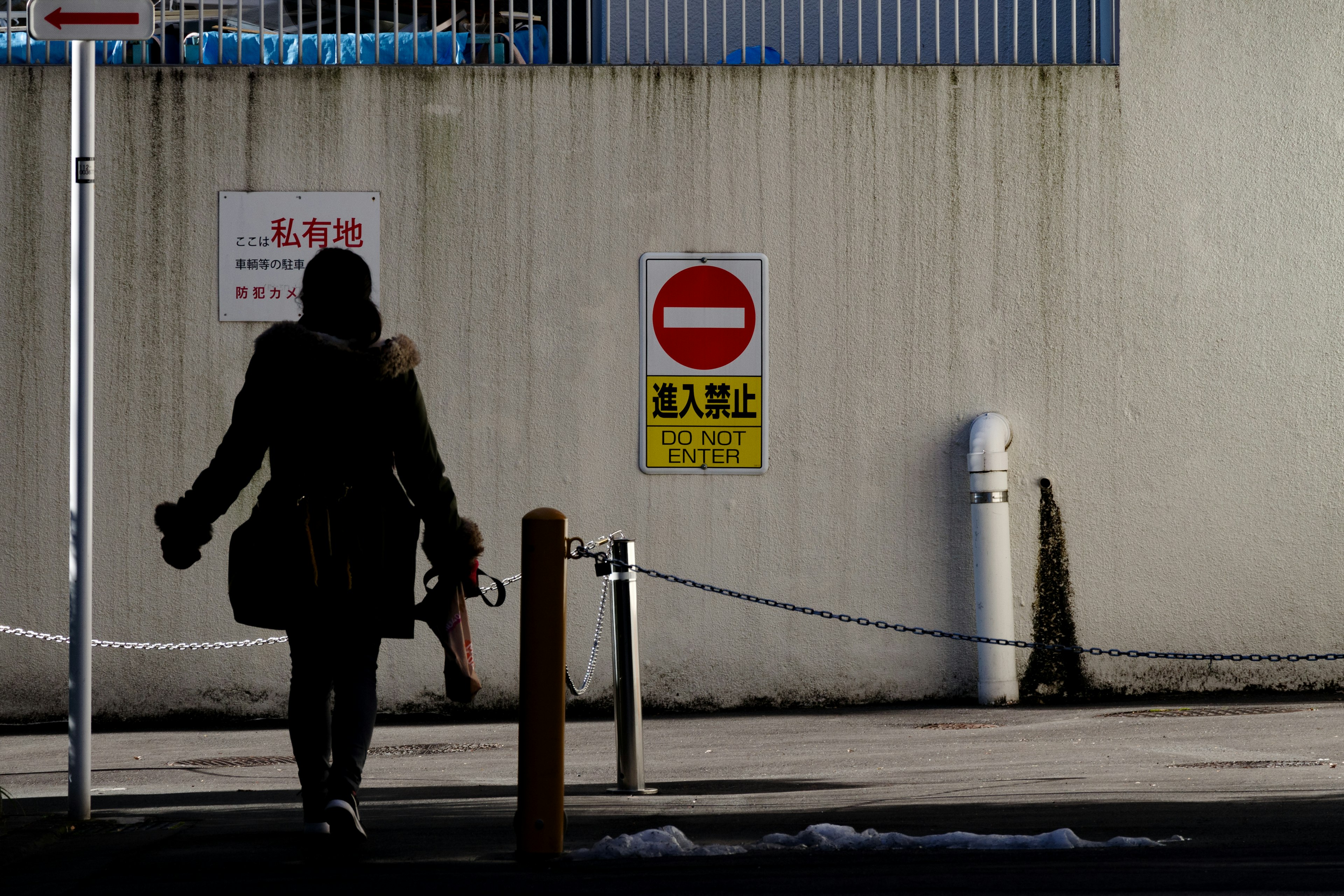 Silhouette of a woman walking alongside a wall with traffic signs