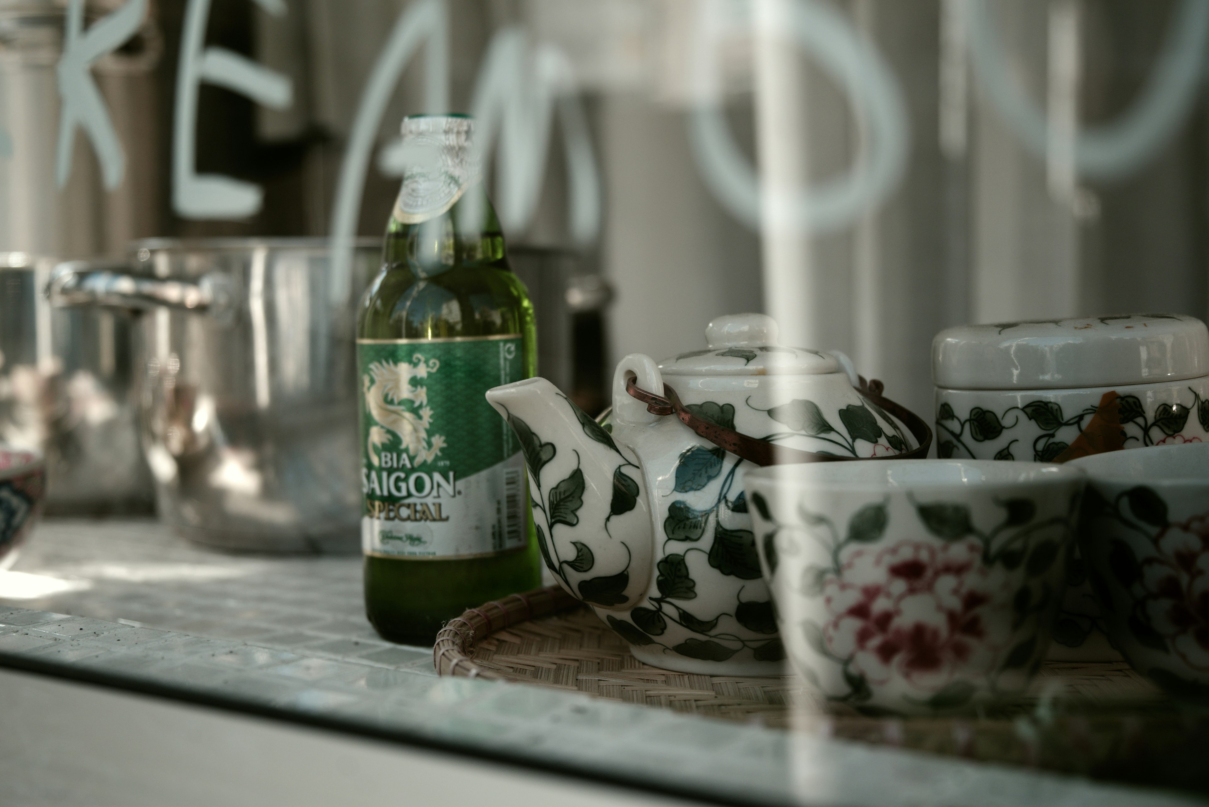 A green beverage bottle and floral tea set displayed behind glass