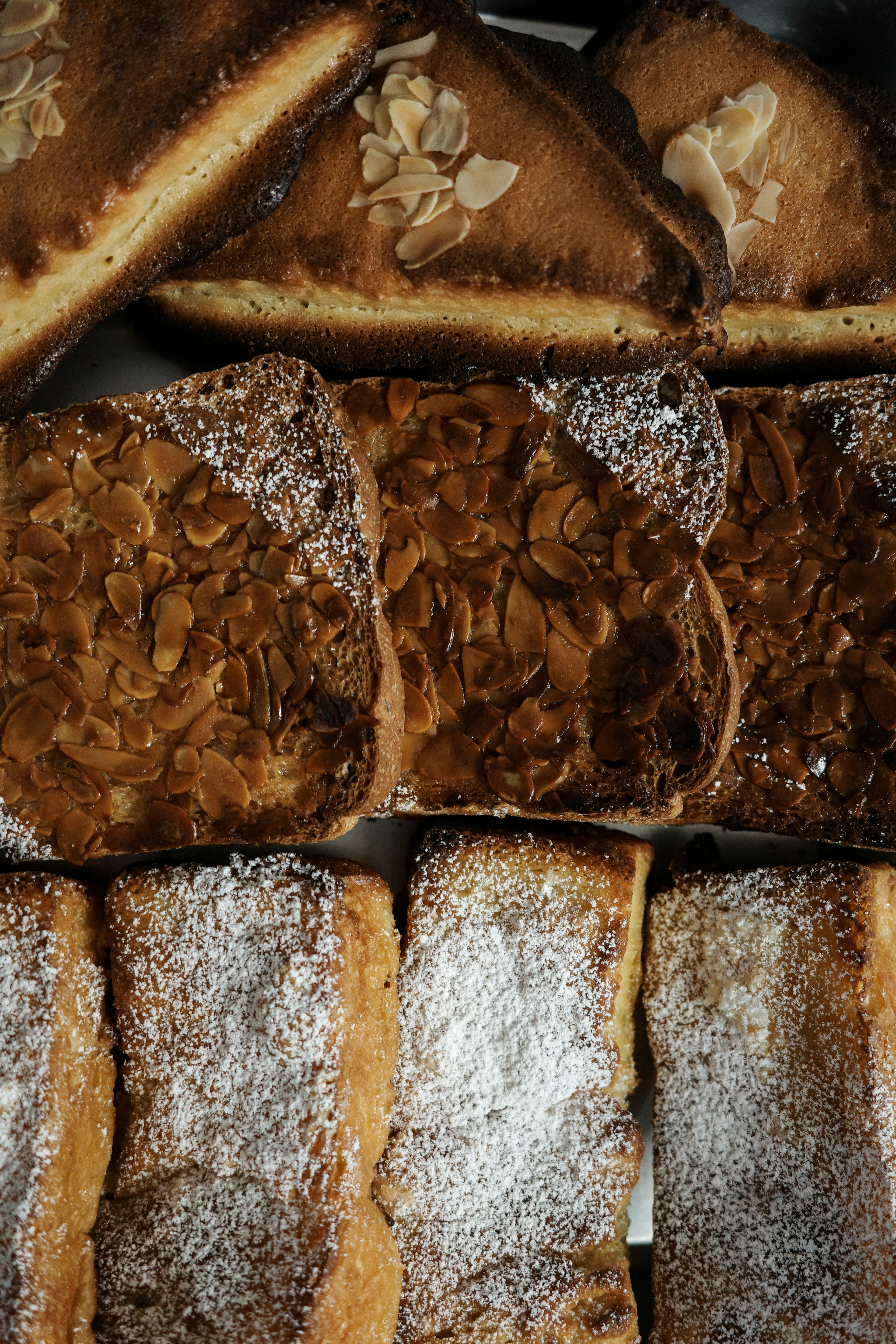 Un assortimento di dolci da forno con pasticcini guarniti con mandorle in cima fette al caramello al centro e pasticcini spolverati di zucchero in basso