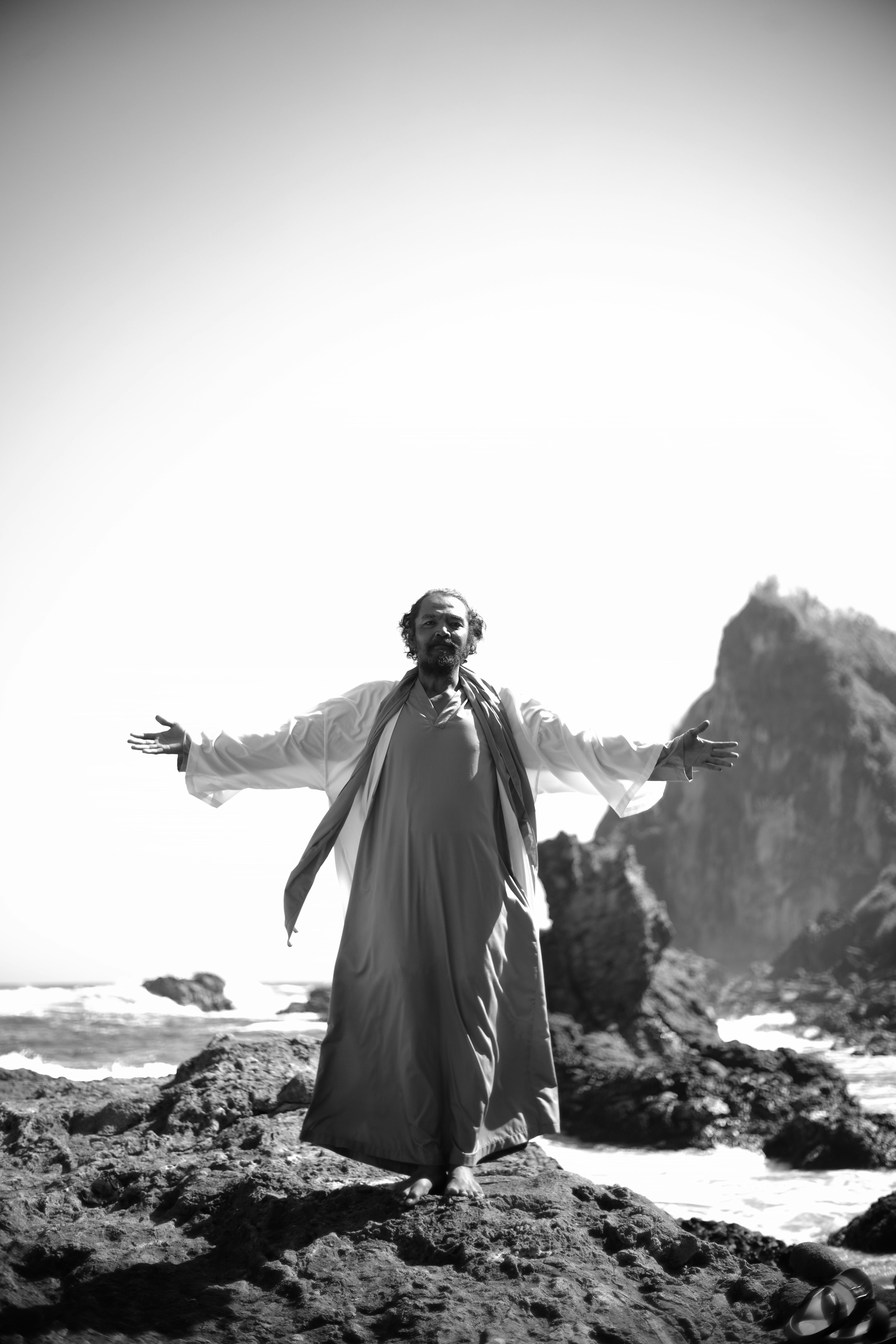 Foto en blanco y negro de un hombre con los brazos extendidos en una costa rocosa