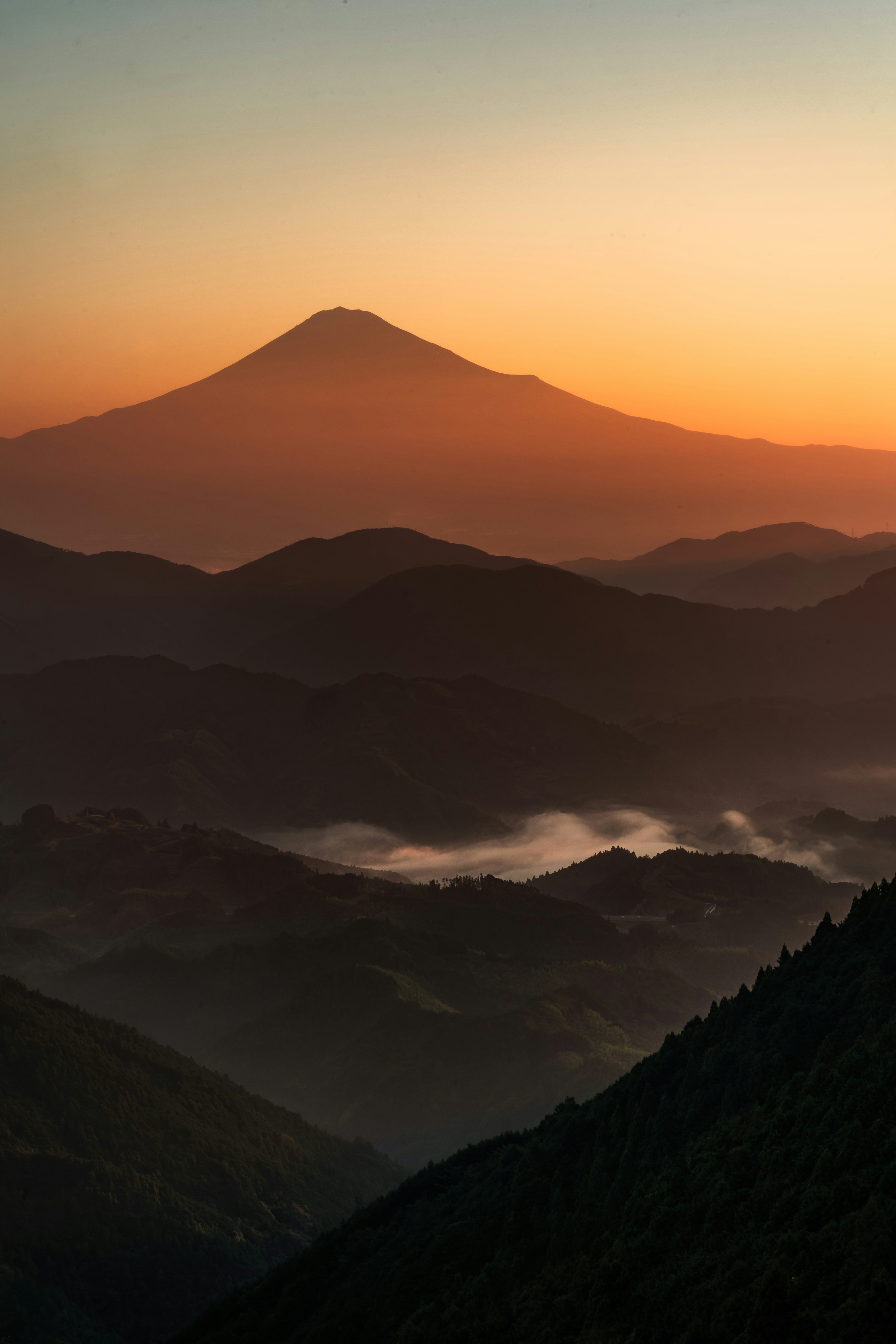 山々のシルエットと美しいオレンジの夕焼けの空 背景には富士山が見える