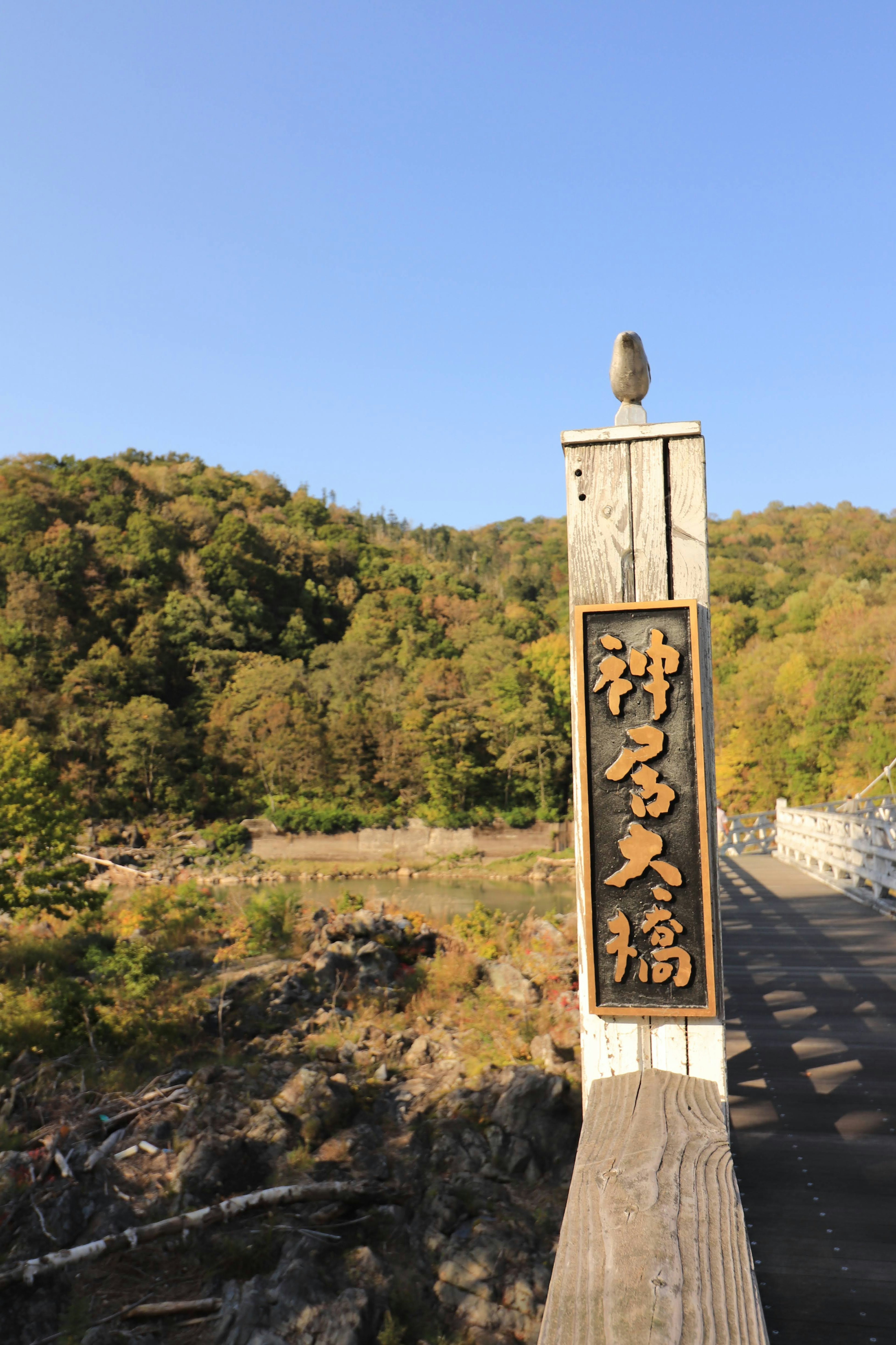 Eine landschaftliche Ansicht mit dem Schild von Kamino Ohashi und grünen Bergen im Hintergrund