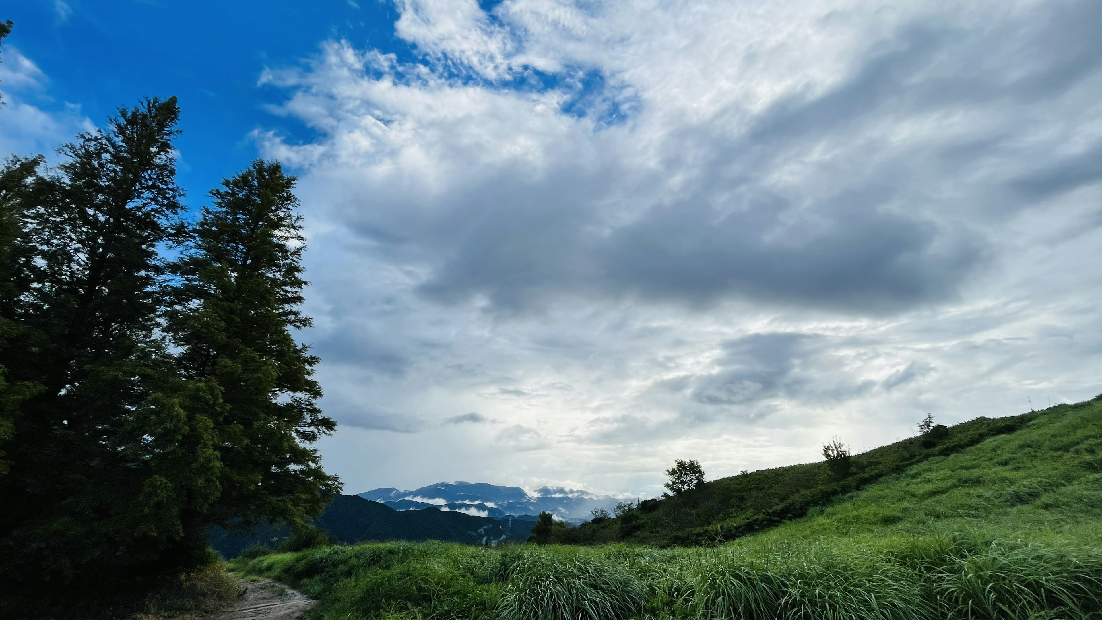 Scenic view of green hills under a blue sky with fluffy white clouds and distant mountains